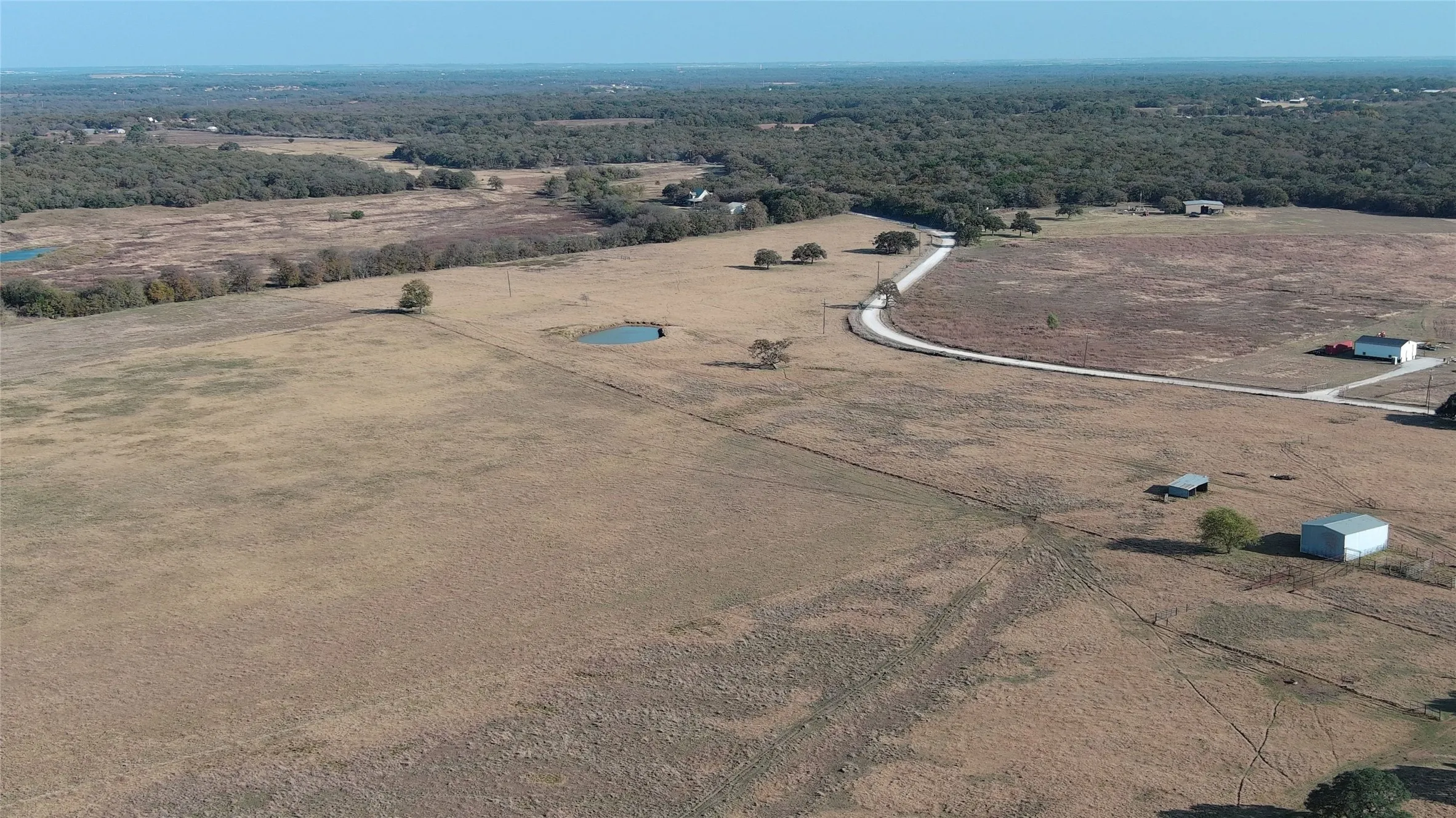 Expansive acreage featuring a winding gravel road, mature trees, two visible ponds, and distant structures