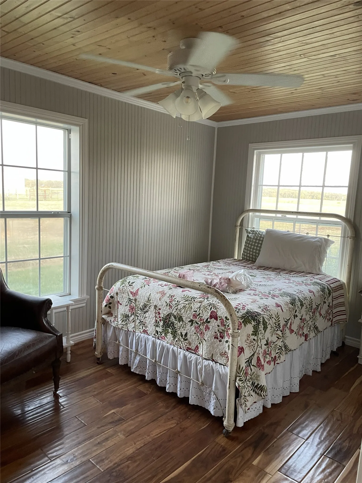 Hardwood flooring complements beadboard wall paneling in this room featuring a wood-paneled ceiling, crown molding, and a ceiling fan with integrated lighting