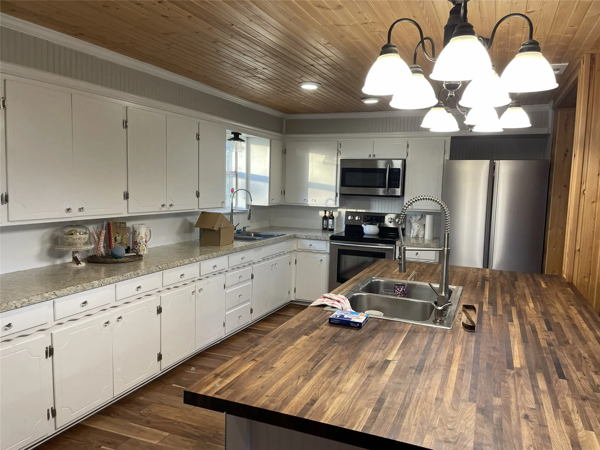 Kitchen featuring wood-finish flooring and ceiling, white cabinetry with light-toned countertops, and a large center island with a double basin sink