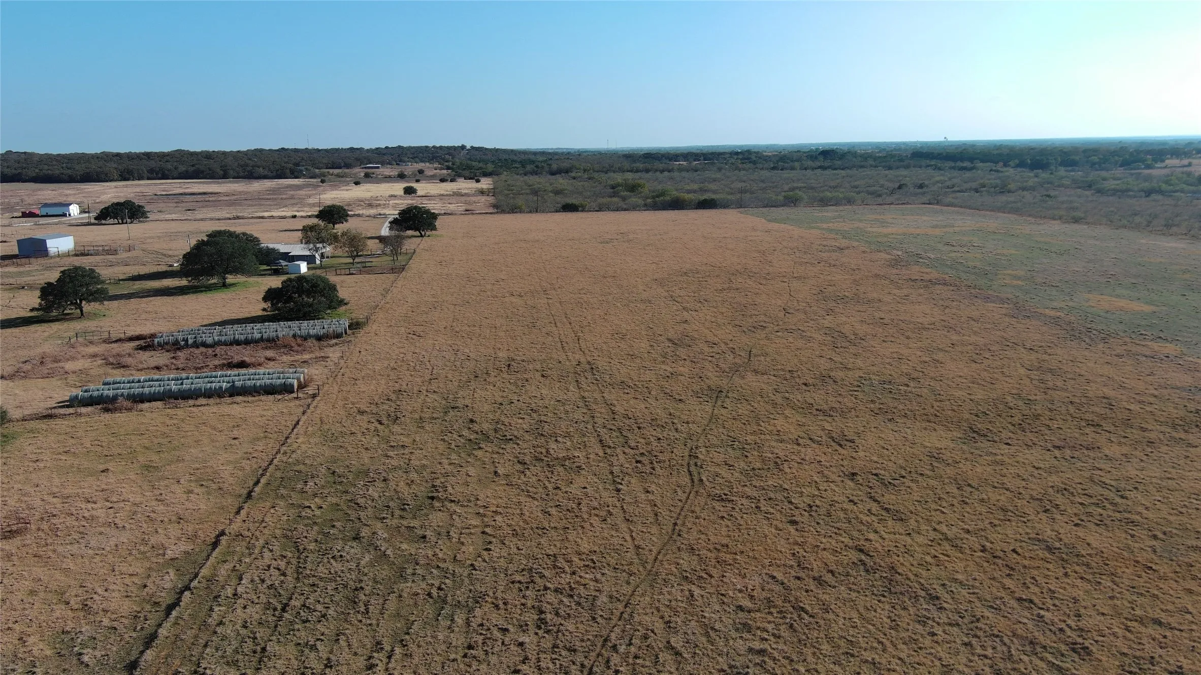 Expansive open fields with distant structures, bordered by a treeline