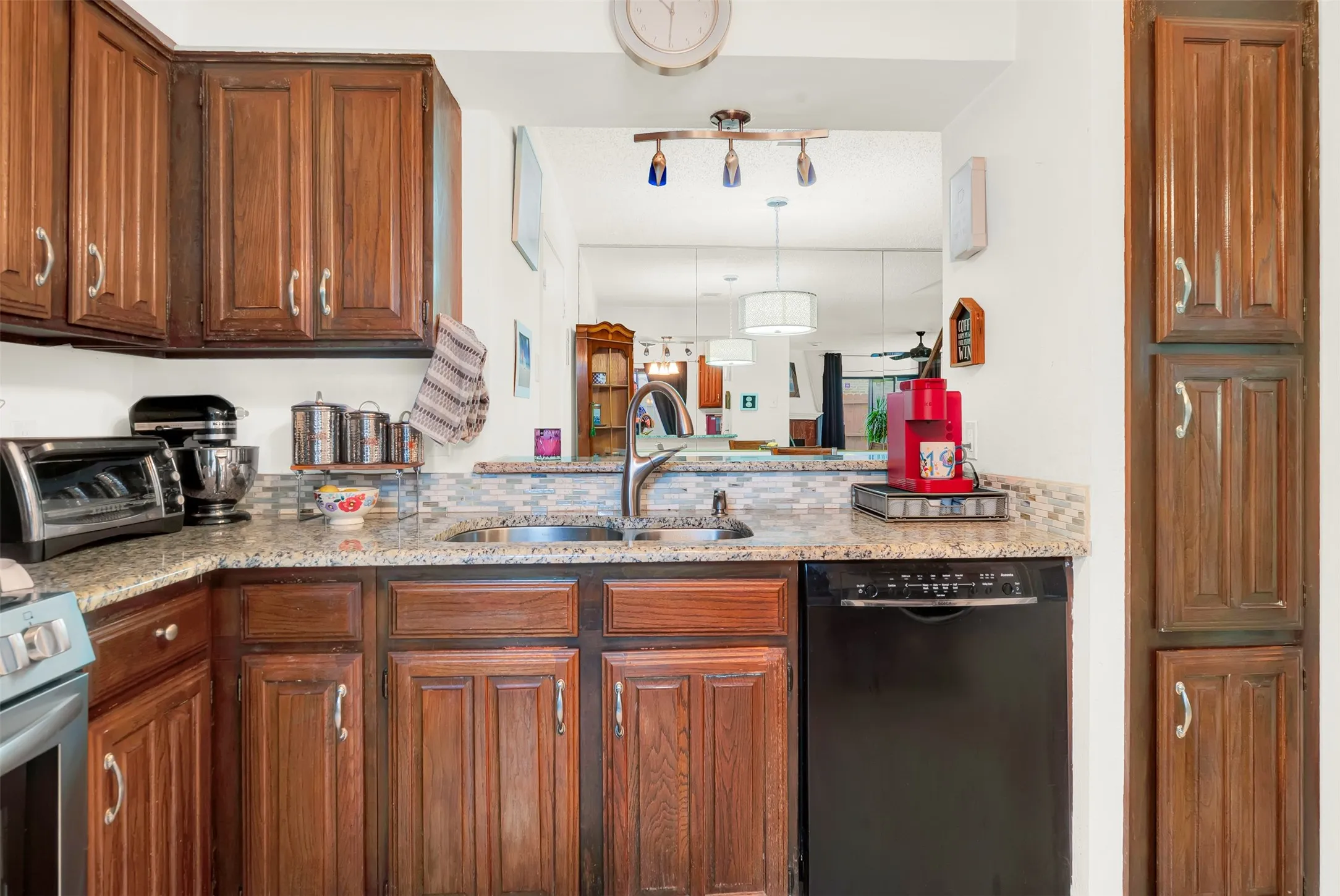 Kitchen featuring wood cabinetry, light-toned granite countertops,  a tiled backsplash and pantry.