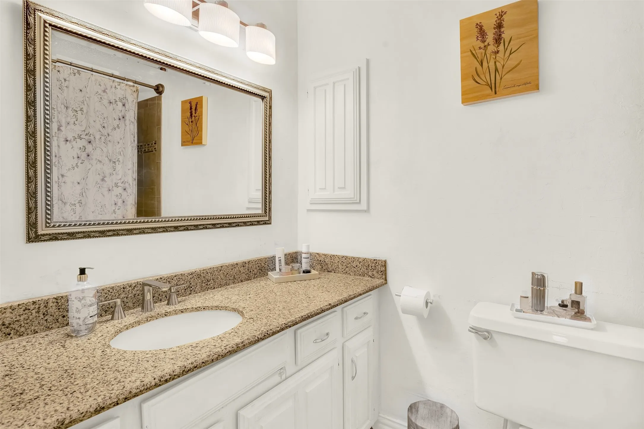 Bathroom featuring a vanity with a light-toned speckled countertop, white cabinetry with silver-toned hardware, an undermount sink, and a framed mirror