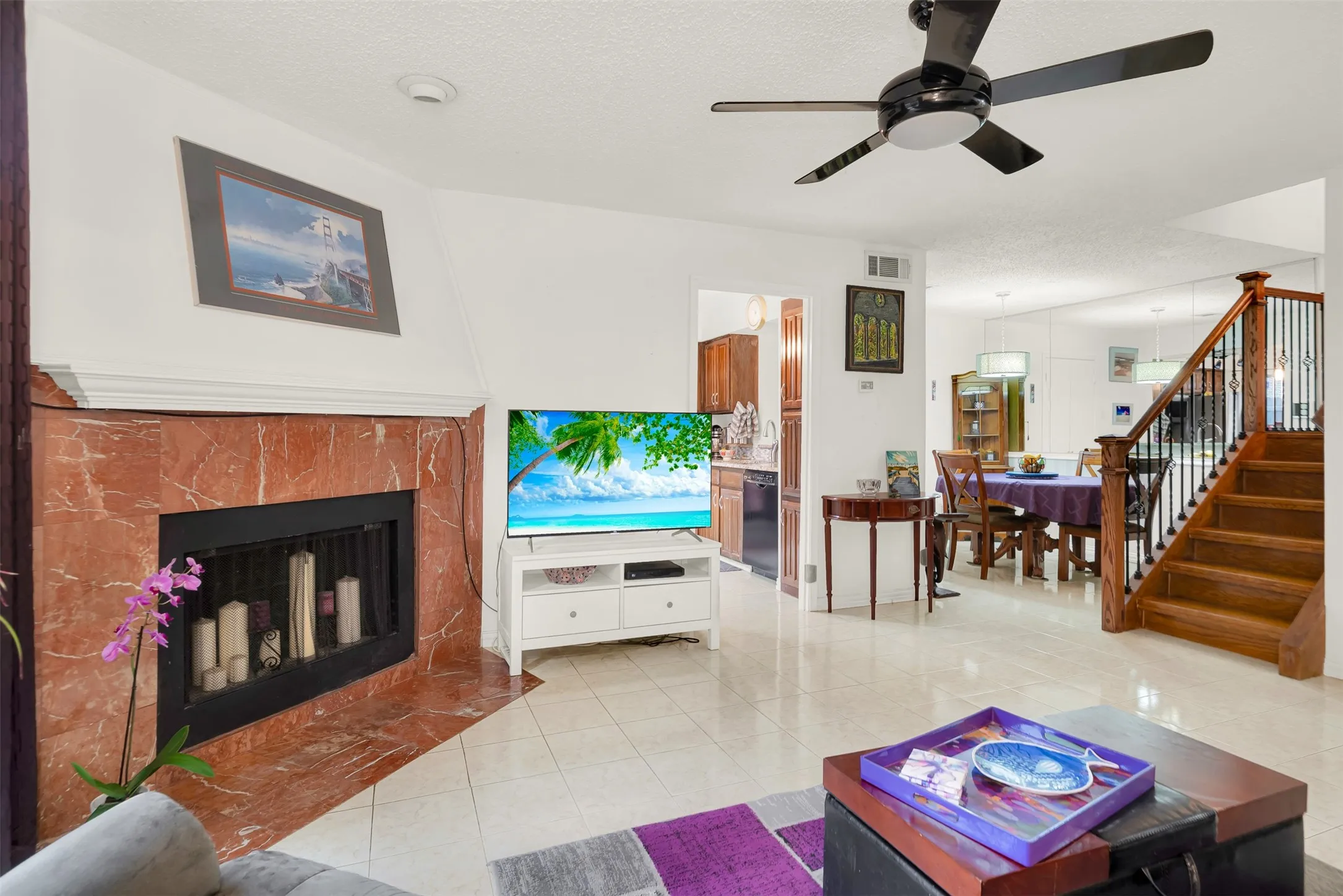 Living area featuring a prominent wood burning fireplace with a red marble surround, tile flooring, and ceiling fan