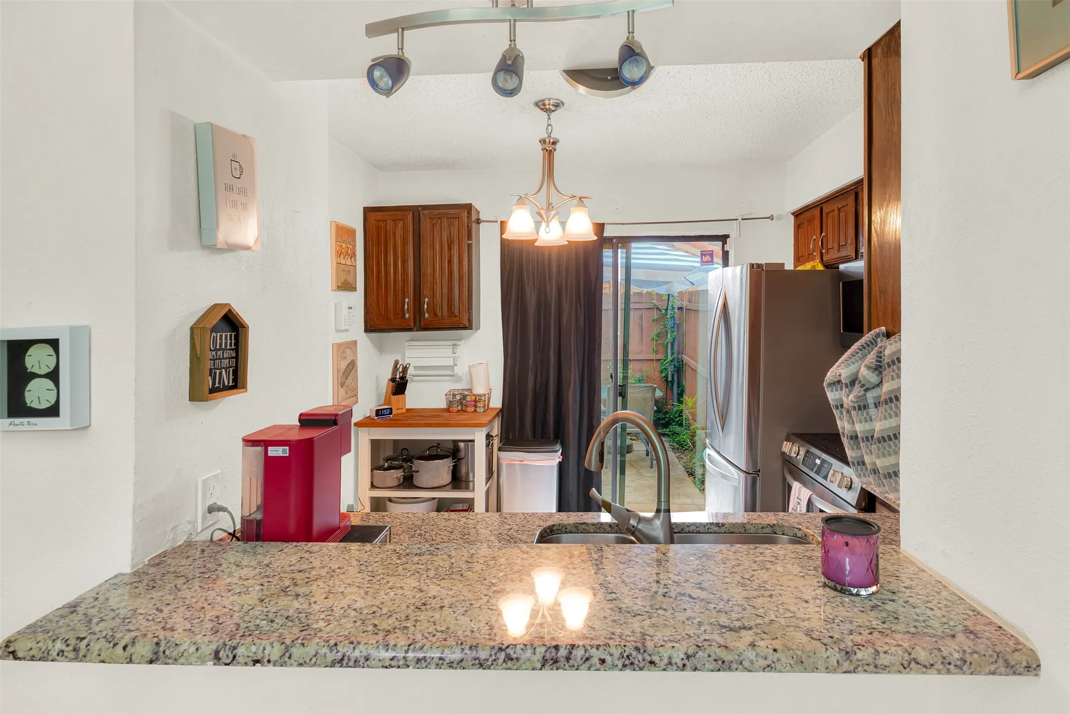 Kitchen featuring granite countertops, undermount sink with gooseneck faucet, wood-finish cabinetry, stainless steel appliances, and sliding glass door access to an outdoor space