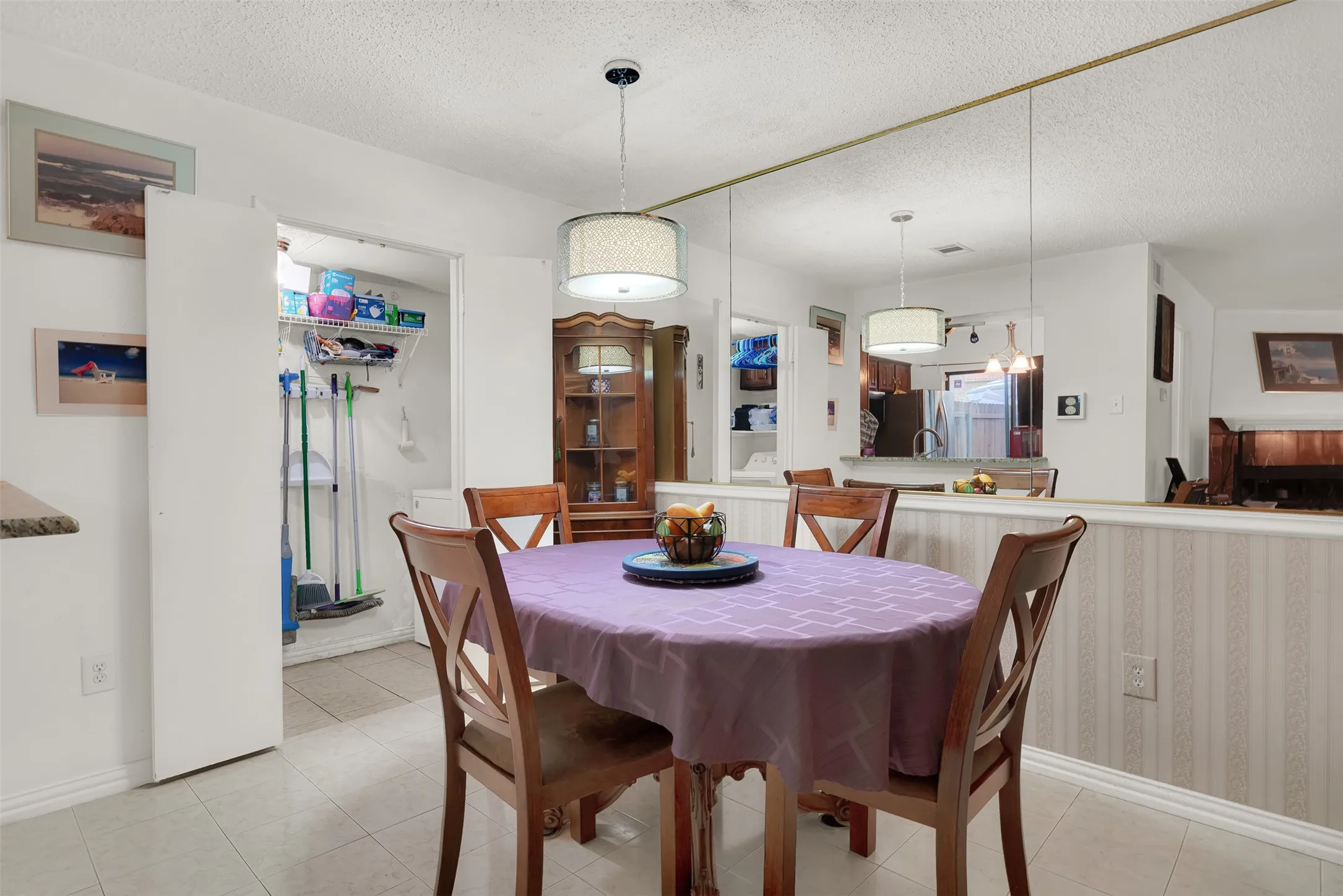 Tiled flooring and pendant light characterize this dining space, featuring a half-wall with textured wallpaper