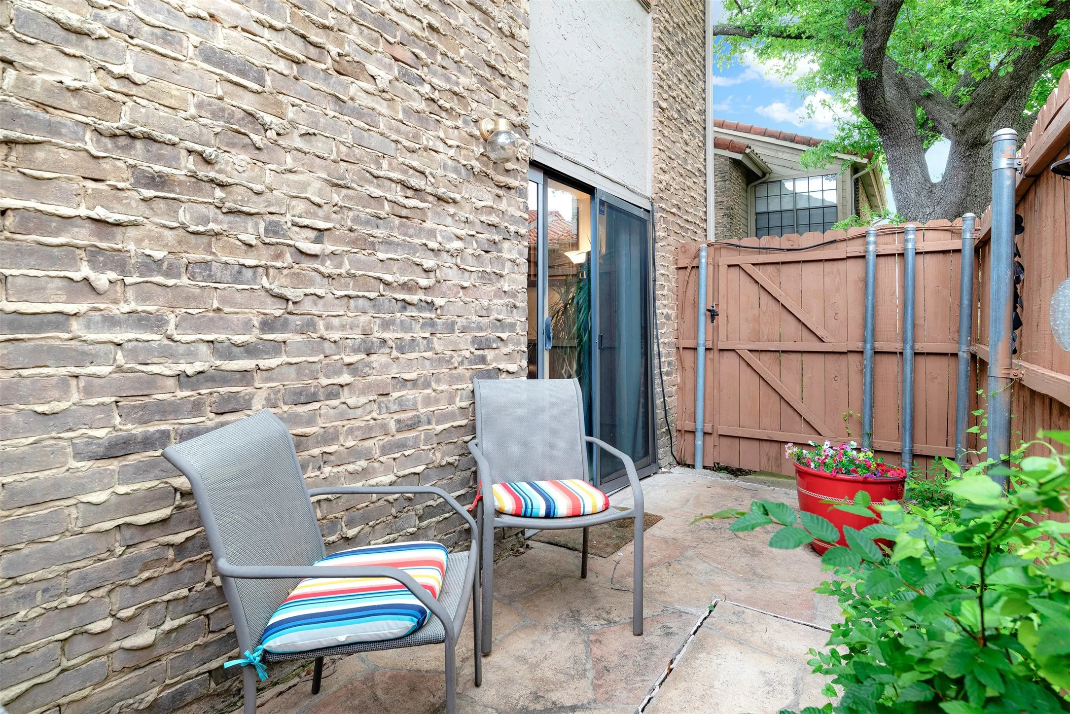 Private stone patio featuring a brick exterior wall, sliding glass door entry, full wooden privacy fence, and mature tree canopy