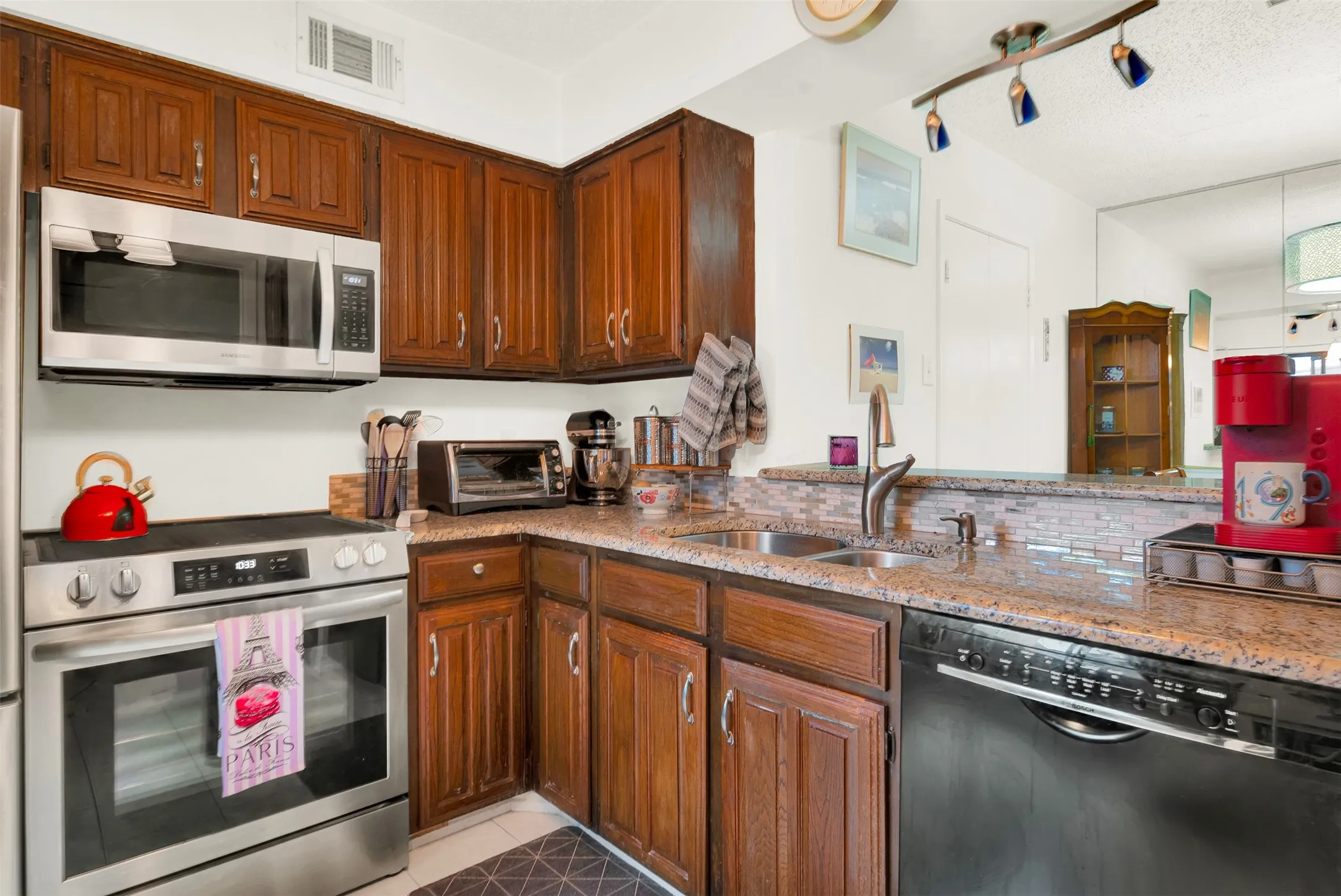 Well-appointed kitchen featuring wood cabinetry, granite countertops, a tile backsplash, and stainless steel appliances