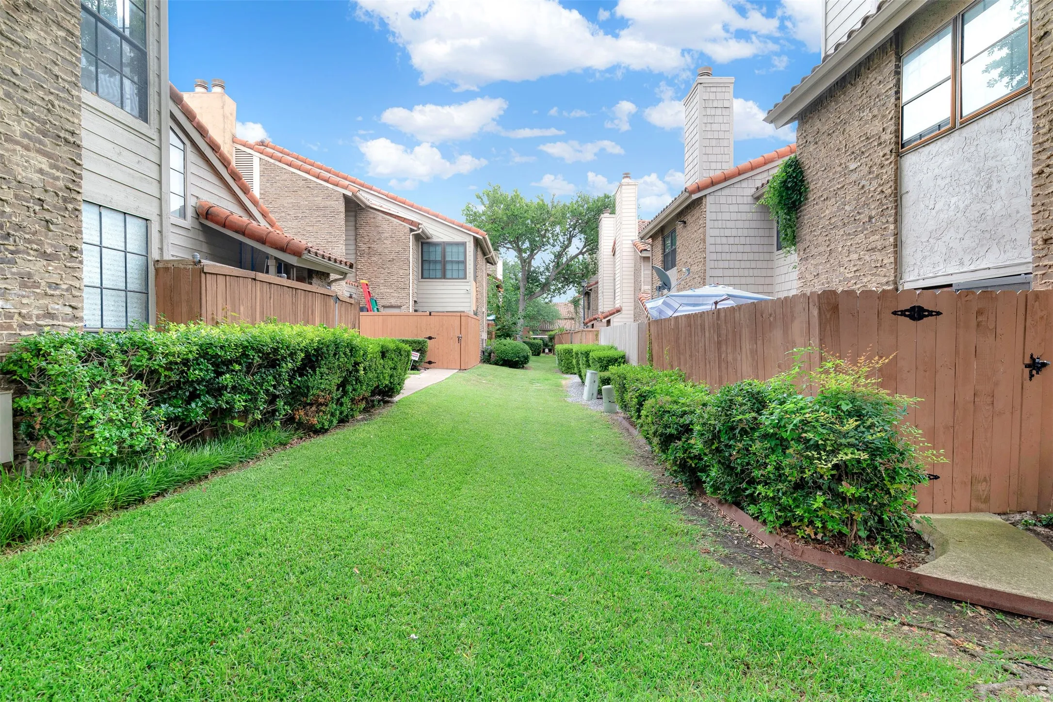 Expansive outdoor space featuring a manicured lawn, established shrubbery, and wood fencing