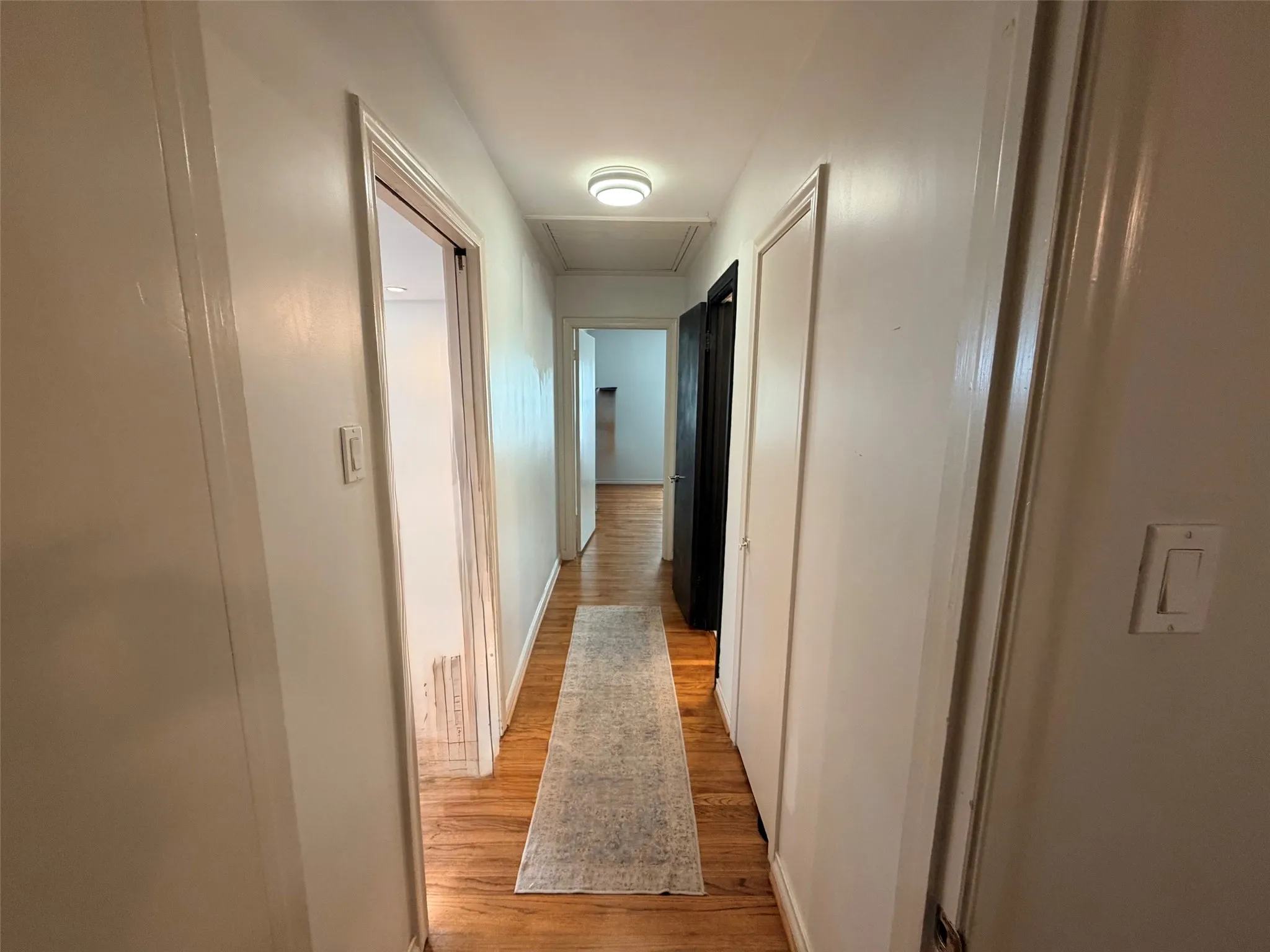 Hallway featuring wood-finish flooring, white painted walls, and ceiling-mounted lighting fixtures