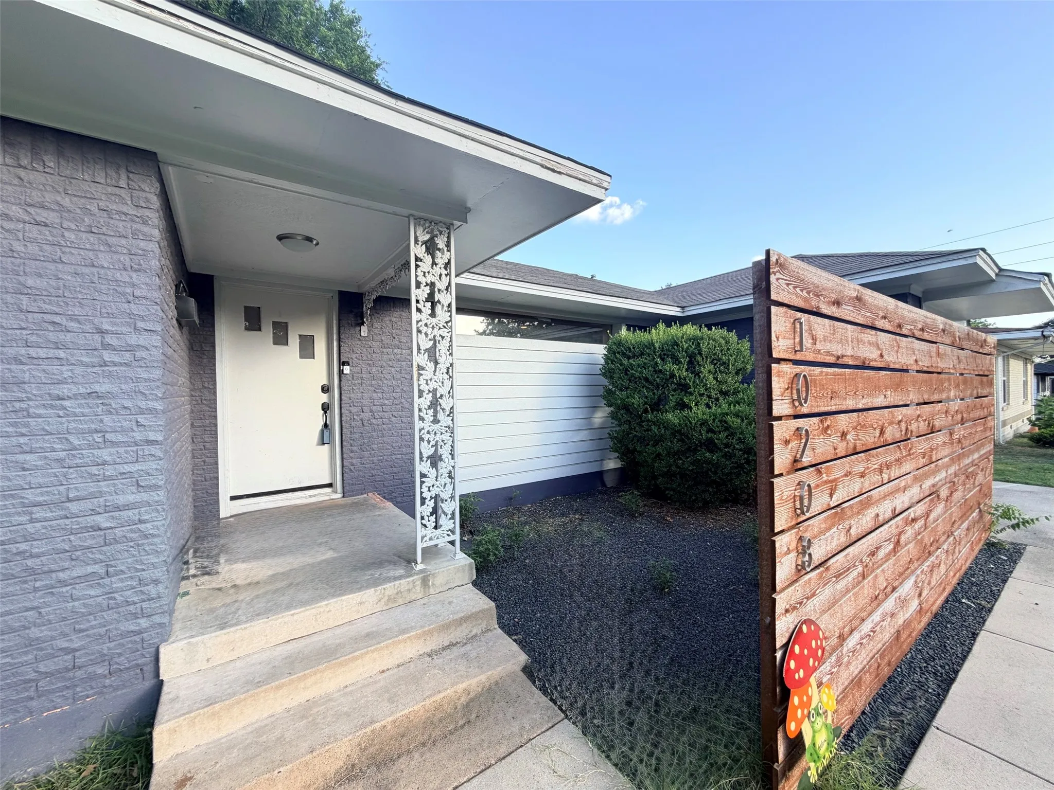 Entryway features a private court yard, rectangular glass inserts, grey textured brick facade and a decorative white metal column
