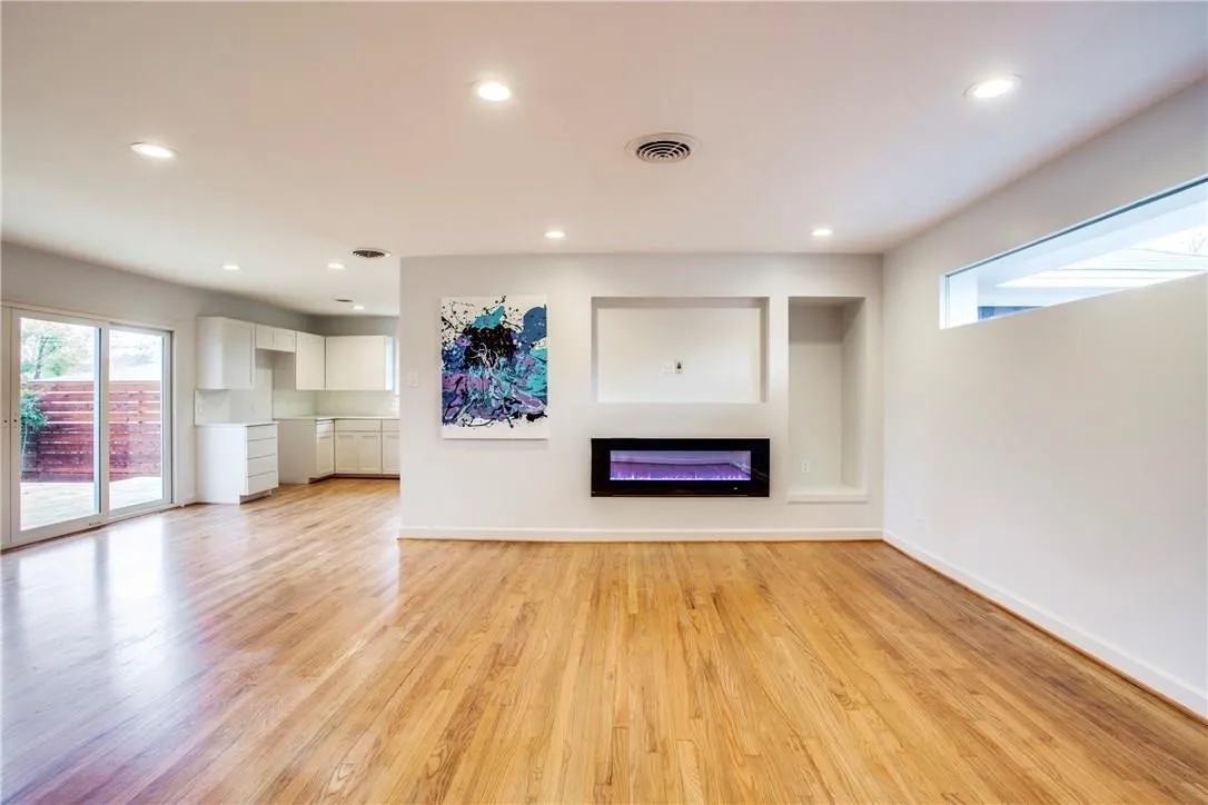 Open-concept living area featuring wood-finish flooring, recessed lighting, and a built-in electric fireplace. Vacant older photo.