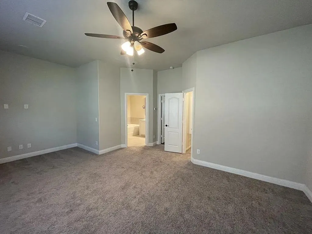Spacious carpeted room featuring a ceiling fan with integrated lighting, painted walls, and white baseboards