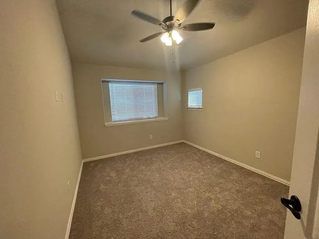 Neutral-toned interior room featuring wall-to-wall carpeting and a ceiling fan with integrated lighting