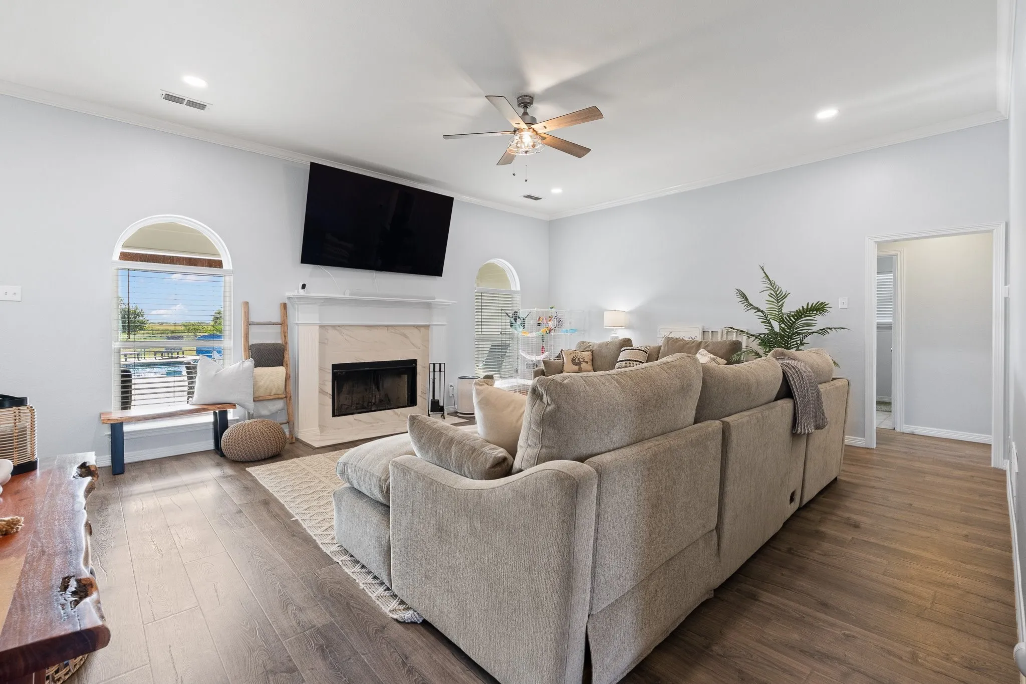 Spacious living area featuring wood-finish flooring, a fireplace with a stone surround and mantel, arched windows, and a ceiling fan