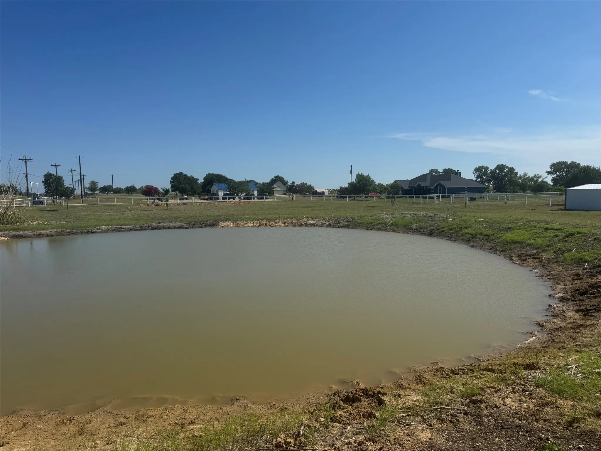 Private pond with natural earthen bank, surrounded by a grassy perimeter and distant fencing