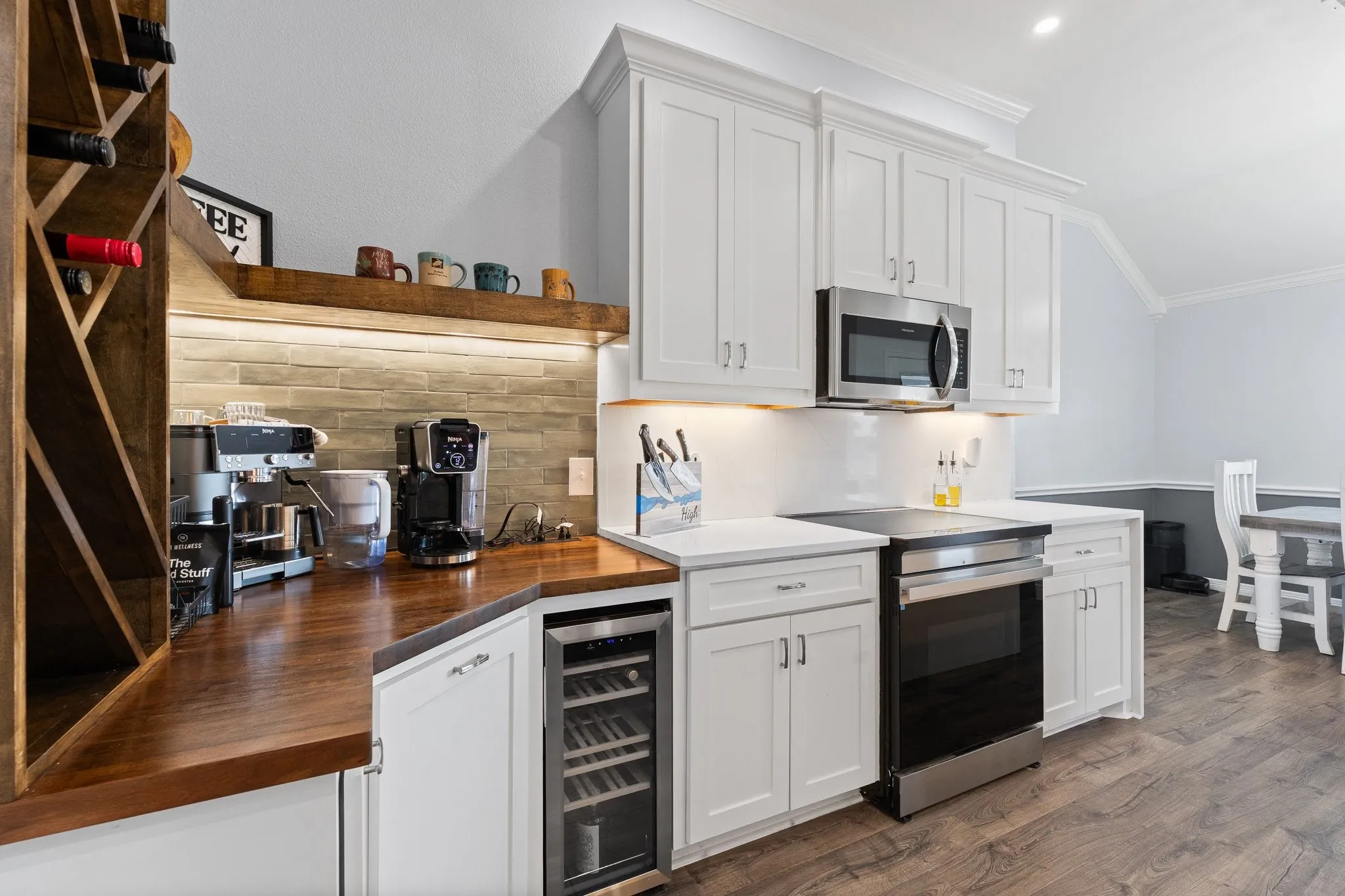 Modern kitchen featuring white cabinetry, stainless steel appliances, a built-in wine cooler, wood-finish flooring, and a stone-tiled backsplash