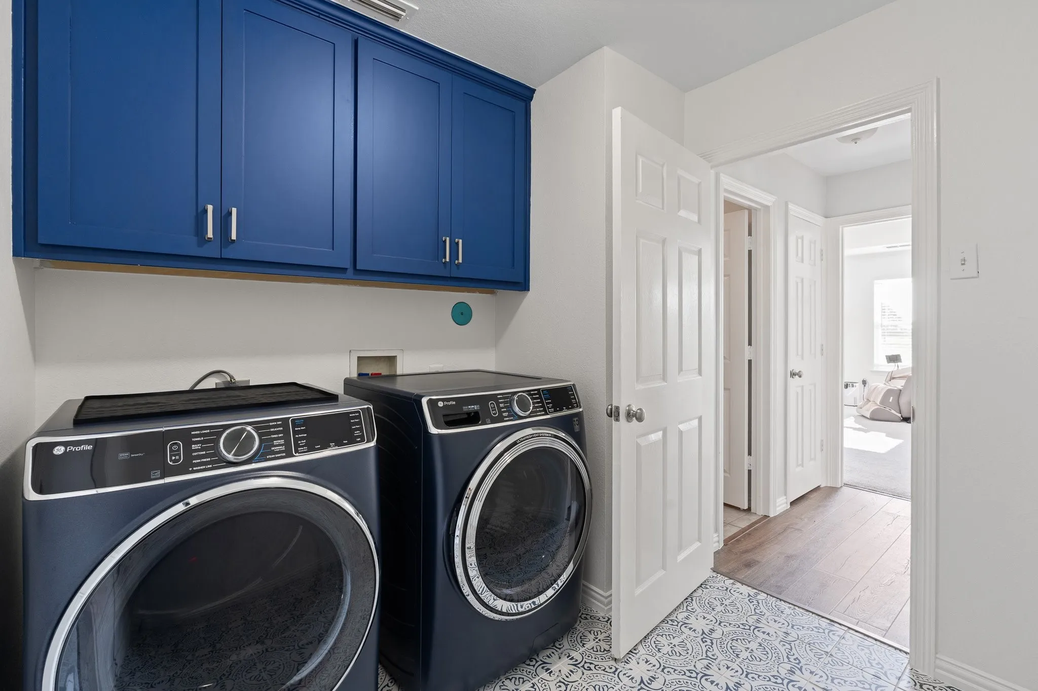Dedicated laundry area featuring blue cabinetry, patterned floor tiling, and white wall paint