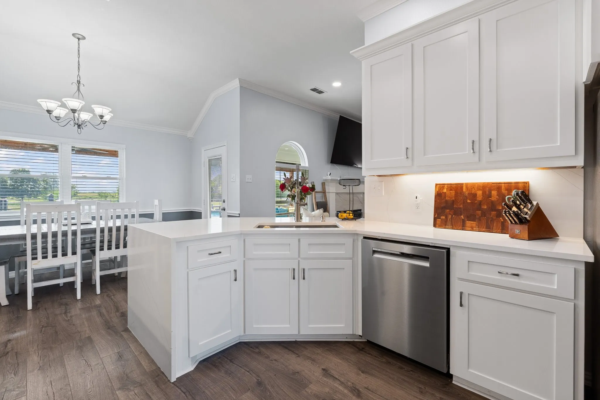 Contemporary kitchen featuring a central island with a sink, white shaker cabinetry, stainless steel dishwasher, wood-finish flooring, and crown molding