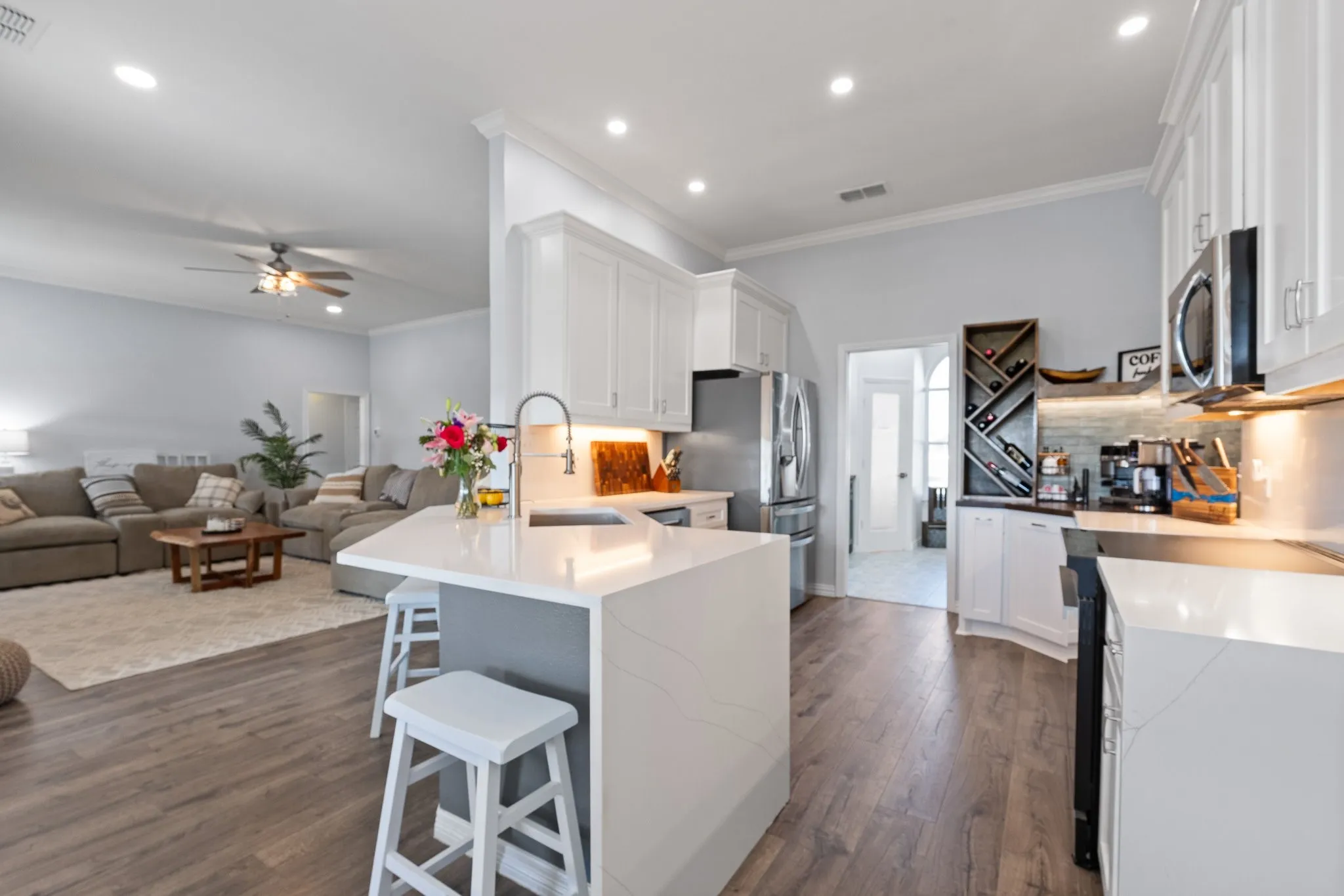 Contemporary kitchen featuring an island with a stainless steel sink and gooseneck faucet, white cabinetry, integrated stainless steel appliances, and wood-finish flooring