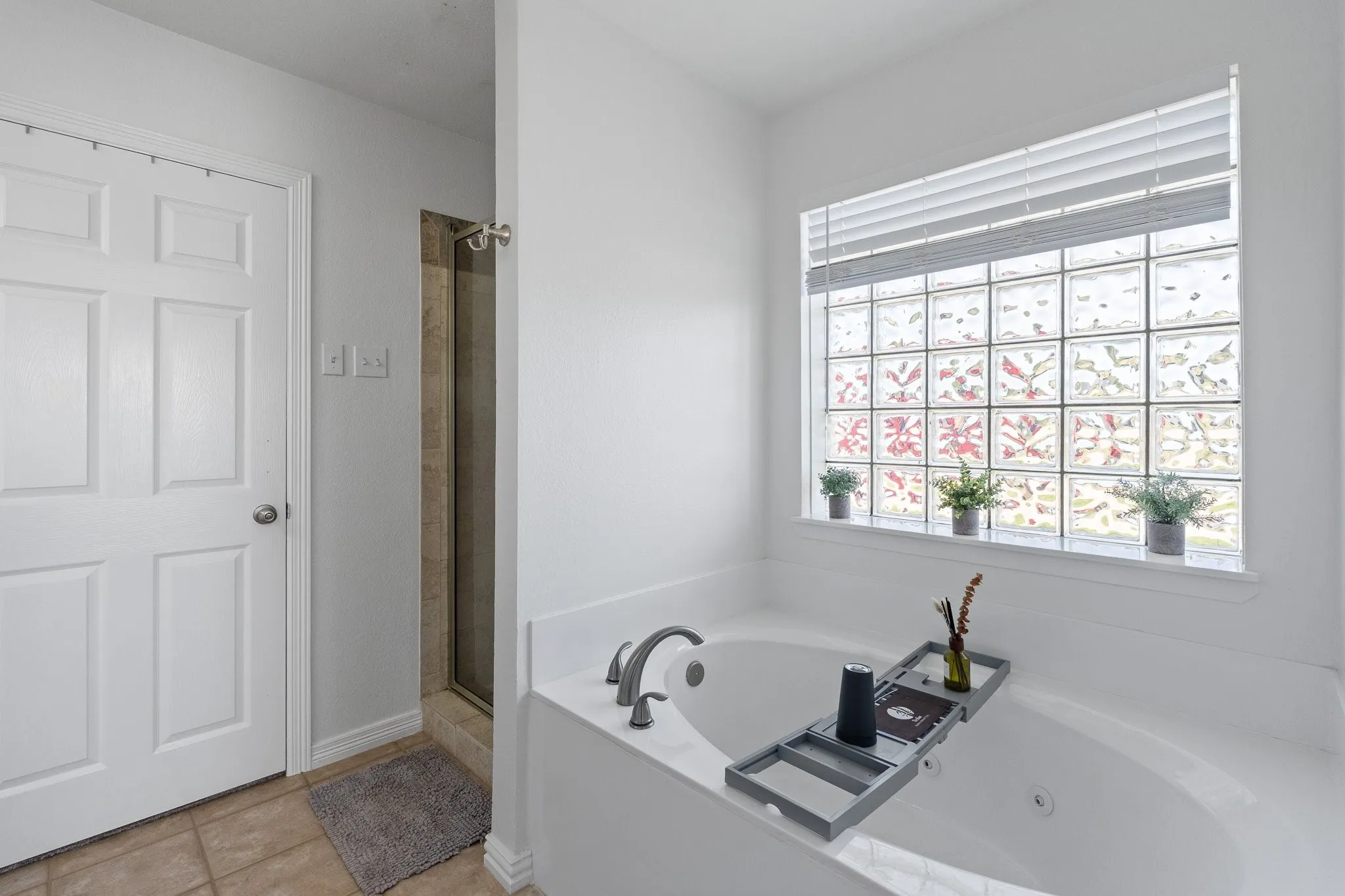 Soaking tub with a dual-handle faucet, glass block window, and white horizontal blinds