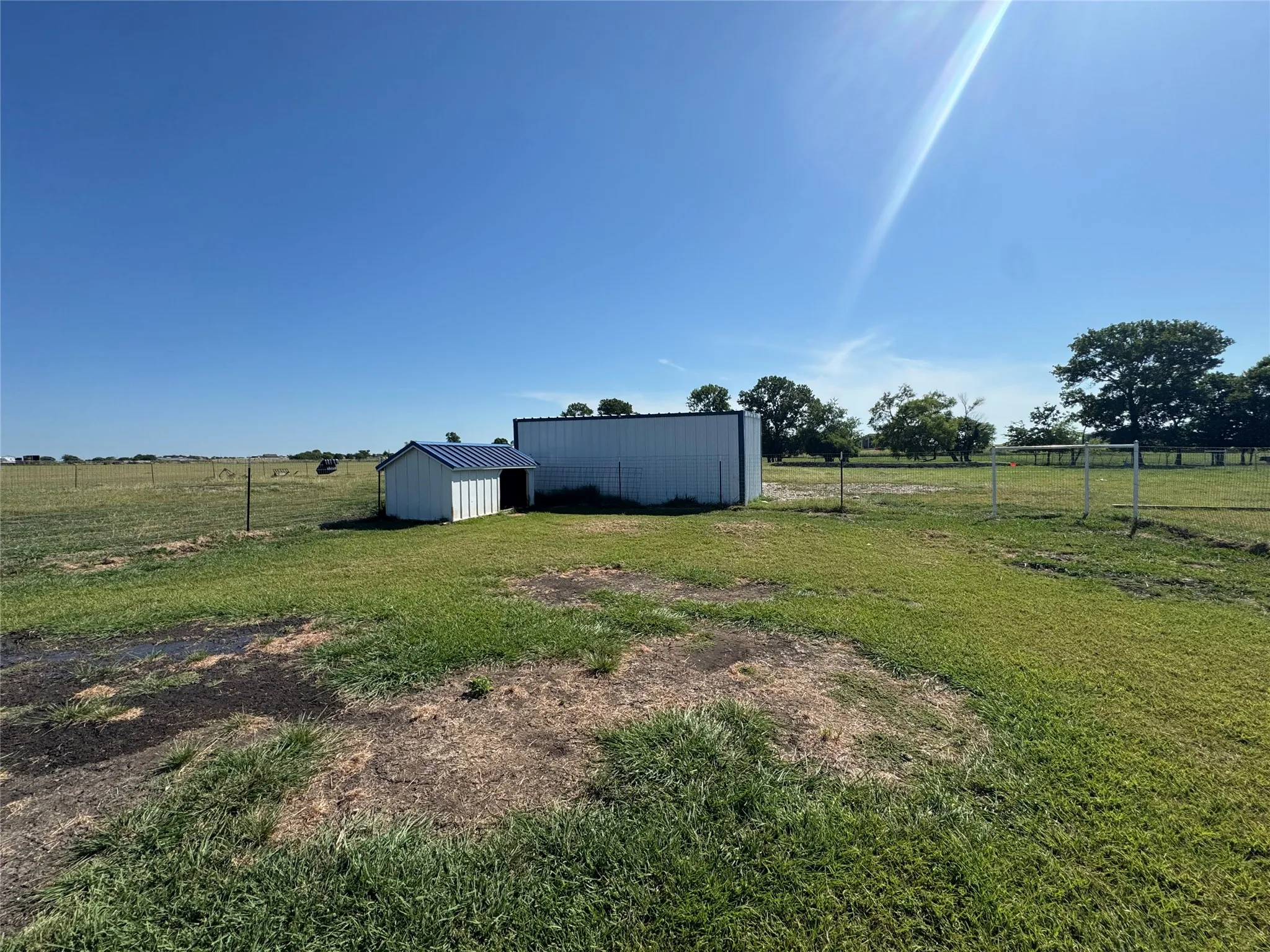 Two outbuildings situated on a grassy landscape with expansive open land