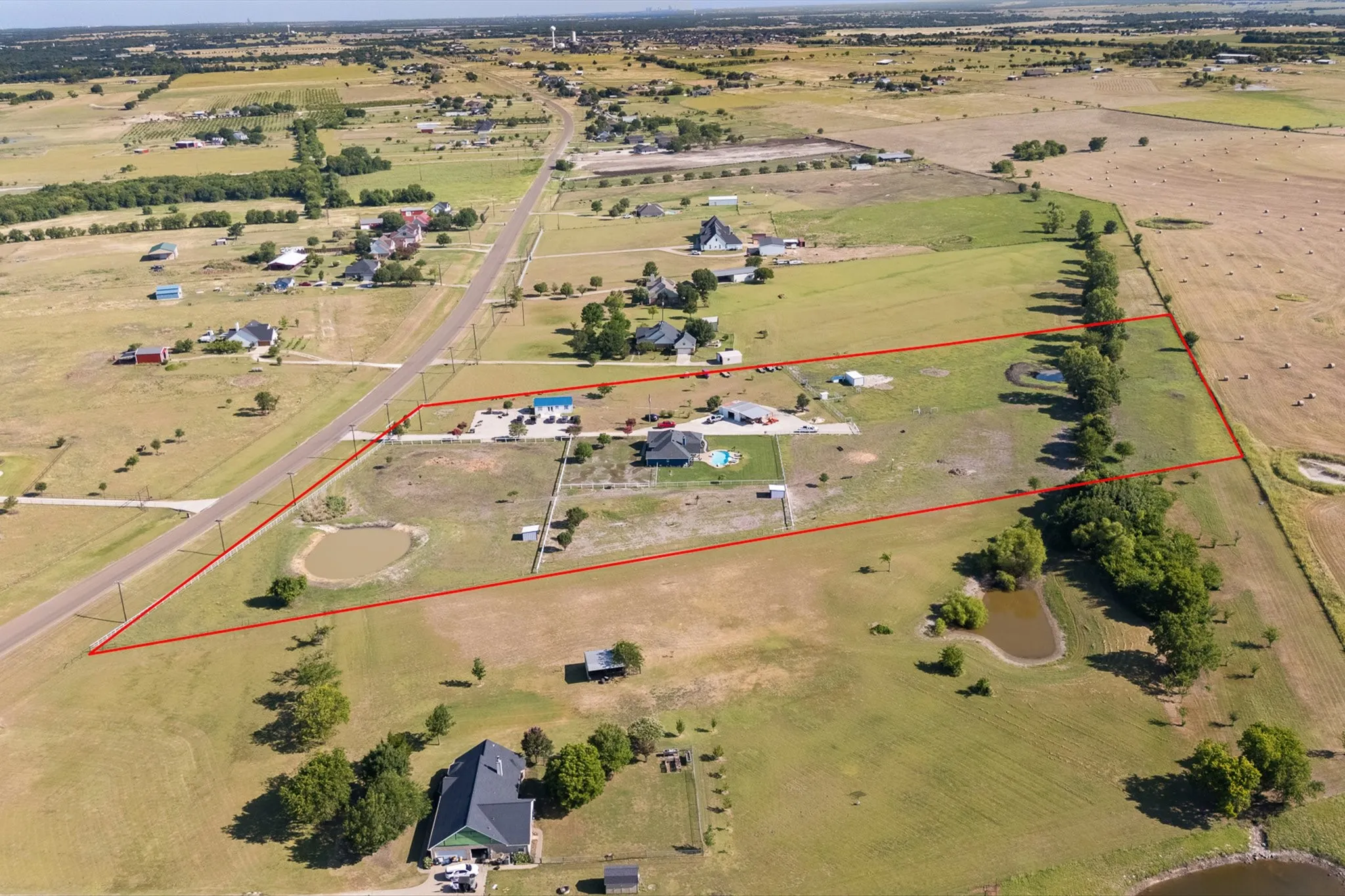 Expansive rural property featuring a primary residence with an outdoor pool, multiple accessory structures, two ponds, and mature tree lines