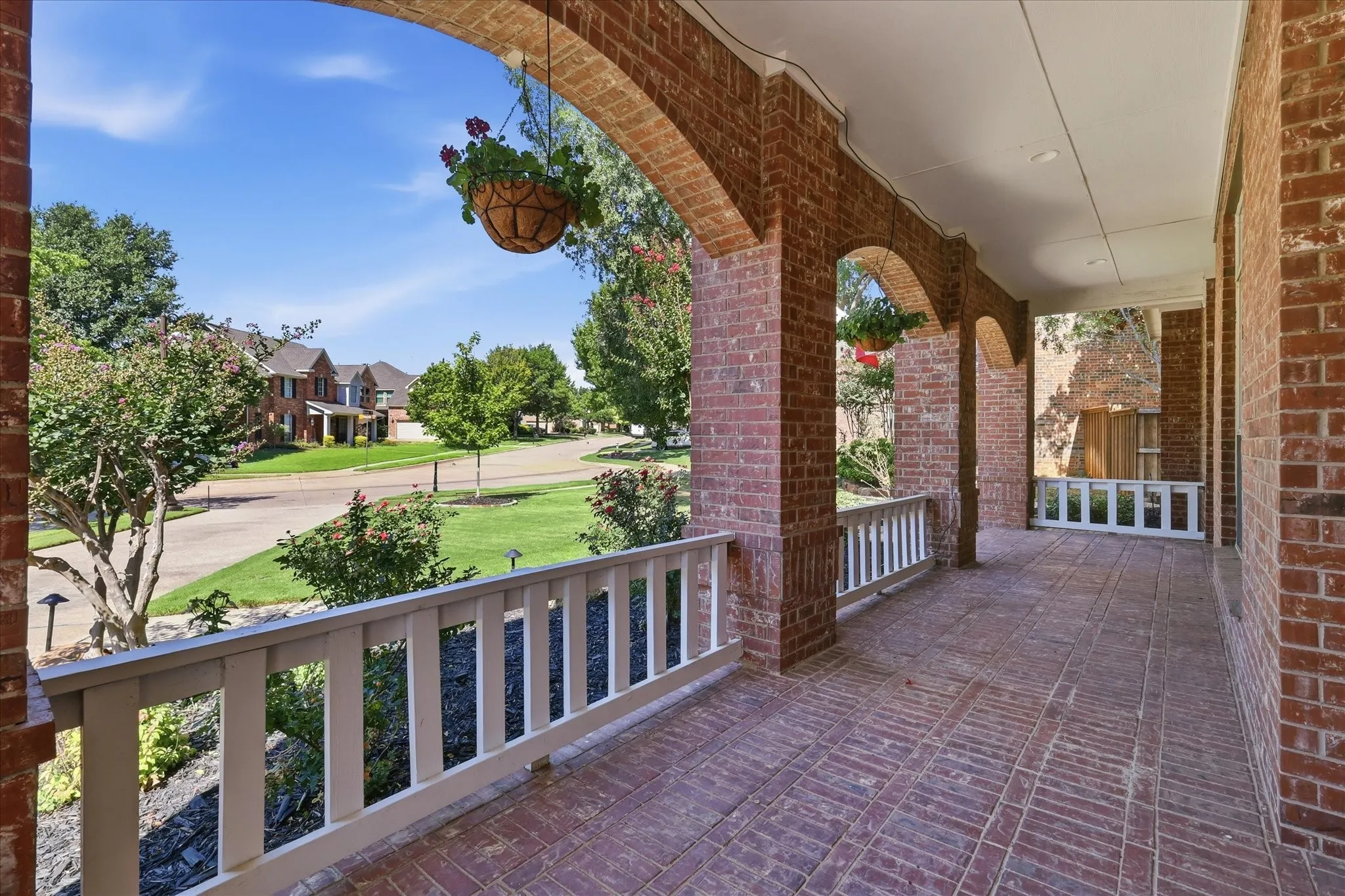 Inviting front porch featuring a brick archway design, brick paver flooring, white railing, and recessed ceiling lighting