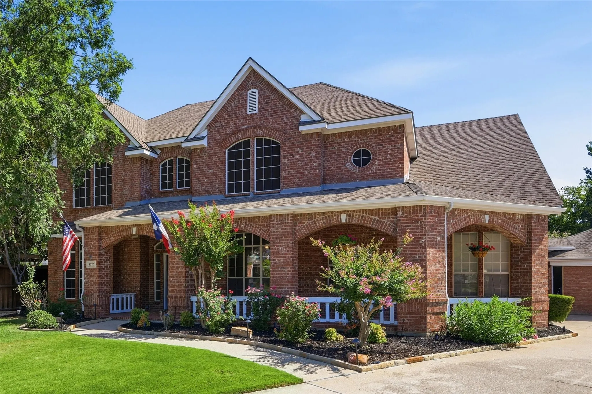 Two-story brick exterior featuring a covered porch with arched openings, multiple gabled rooflines, and a circular window accent