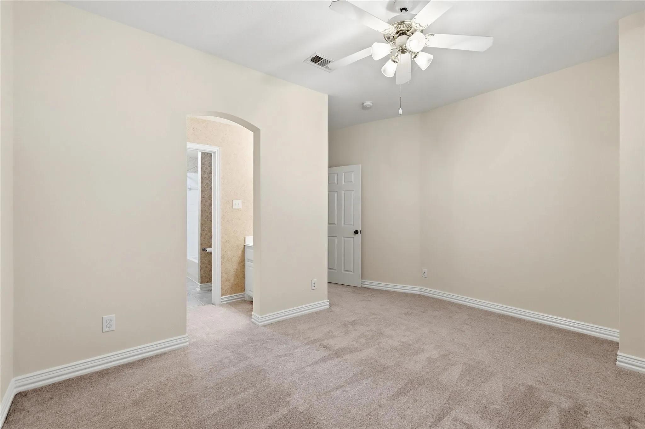 Bedroom featuring two arched doorway with light beige wall paint, gray carpet flooring, white baseboards, and a ceiling fan