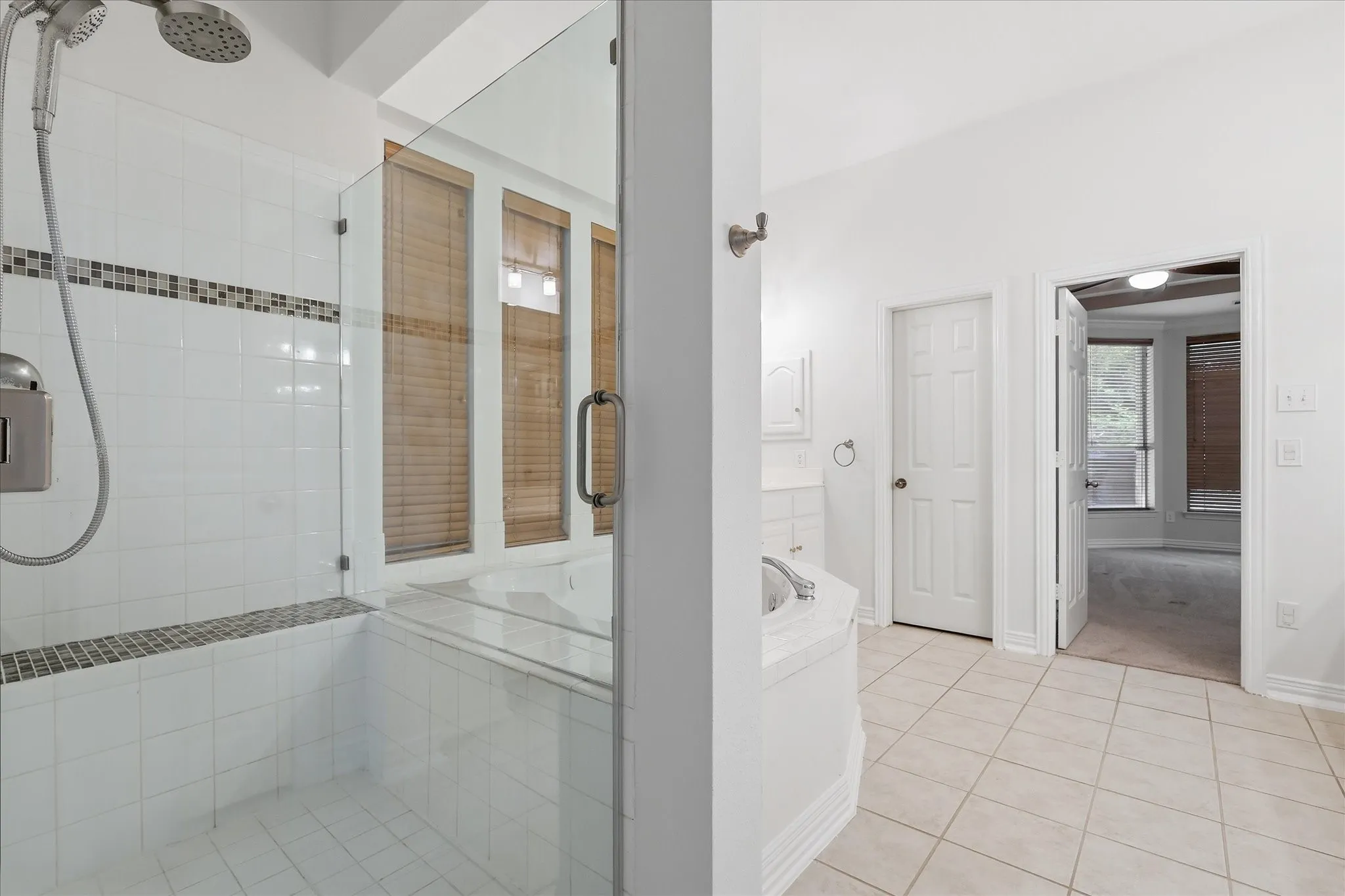 Primary bathroom featuring a corner jetted tub, a glass-enclosed shower with tile surround, wood blinds, and tile flooring