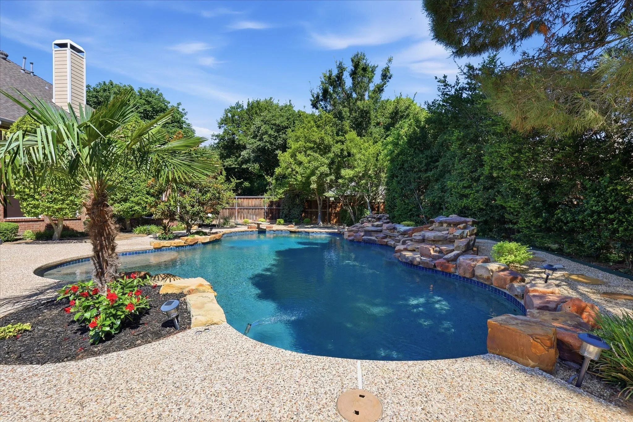 Freeform swimming pool featuring a rock waterfall, flagstone coping, and a pebble-finish deck