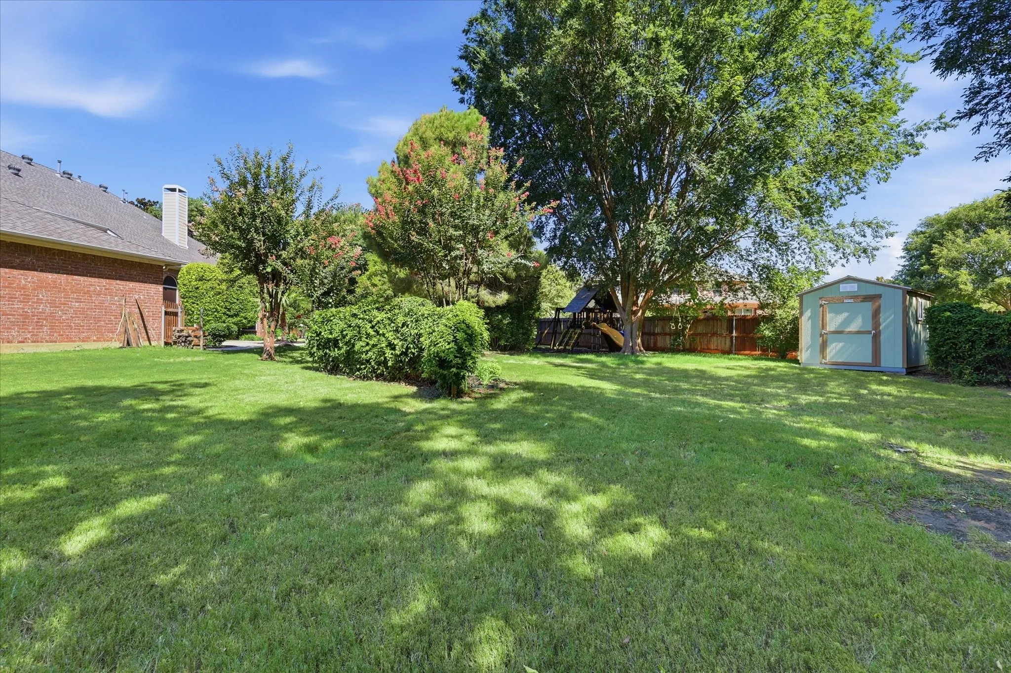 Expansive backyard featuring a lush lawn, mature trees, a storage shed, and a privacy fence