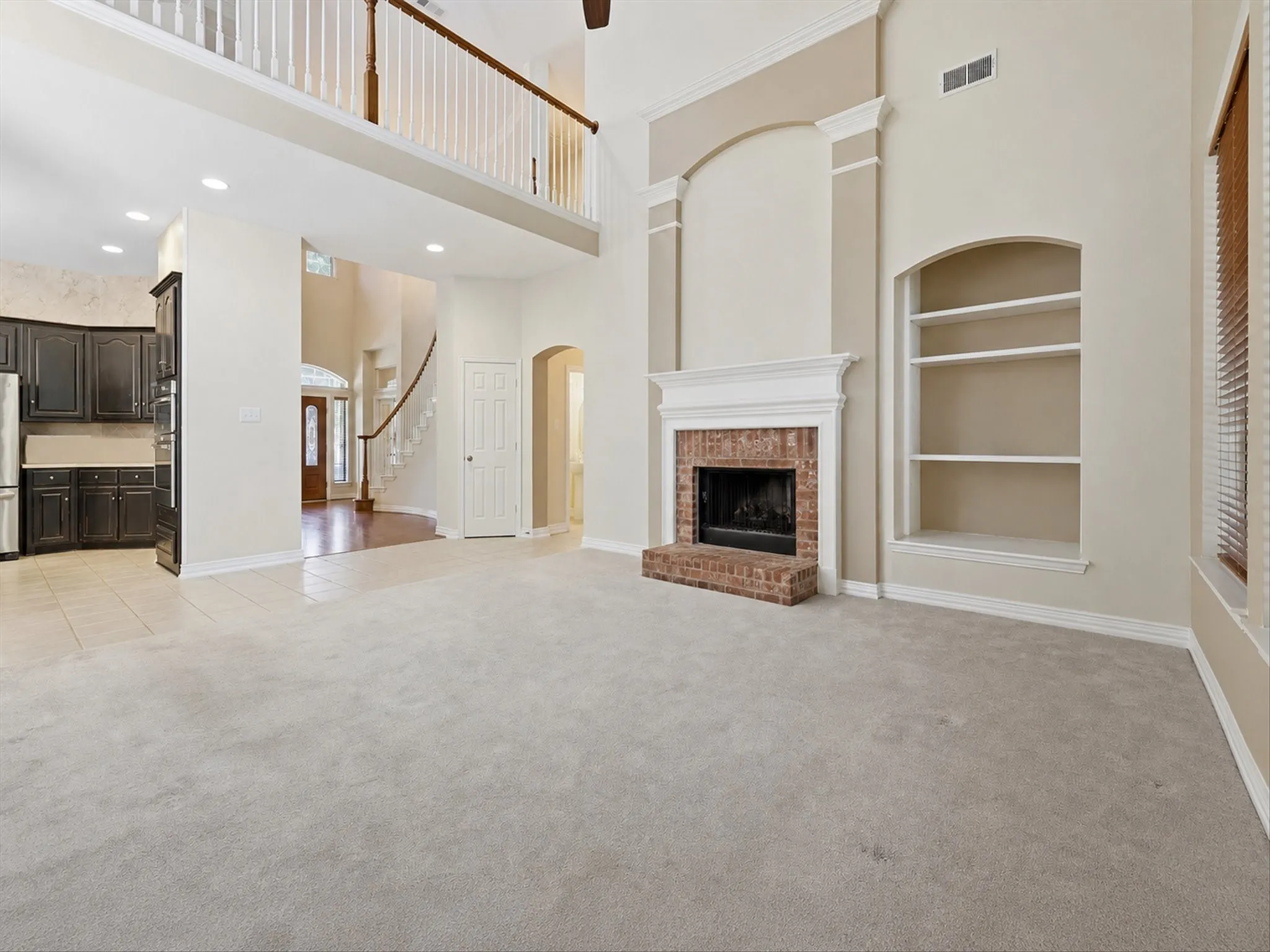 Spacious living area featuring a brick fireplace with a white mantel, built-in shelving, high ceilings, and light-toned carpeting