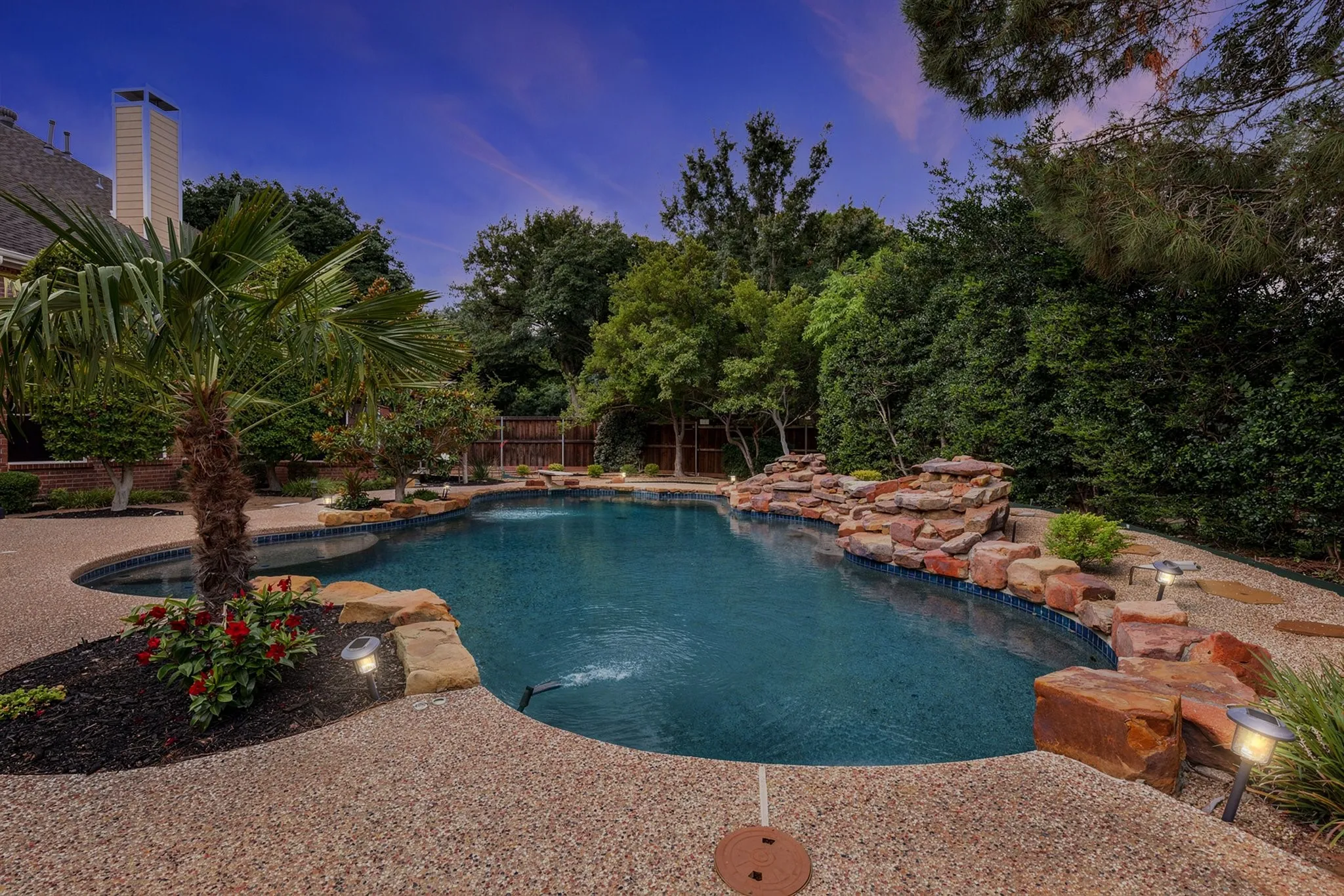 Freeform swimming pool with a rock waterfall feature, integrated spa, and aggregate decking