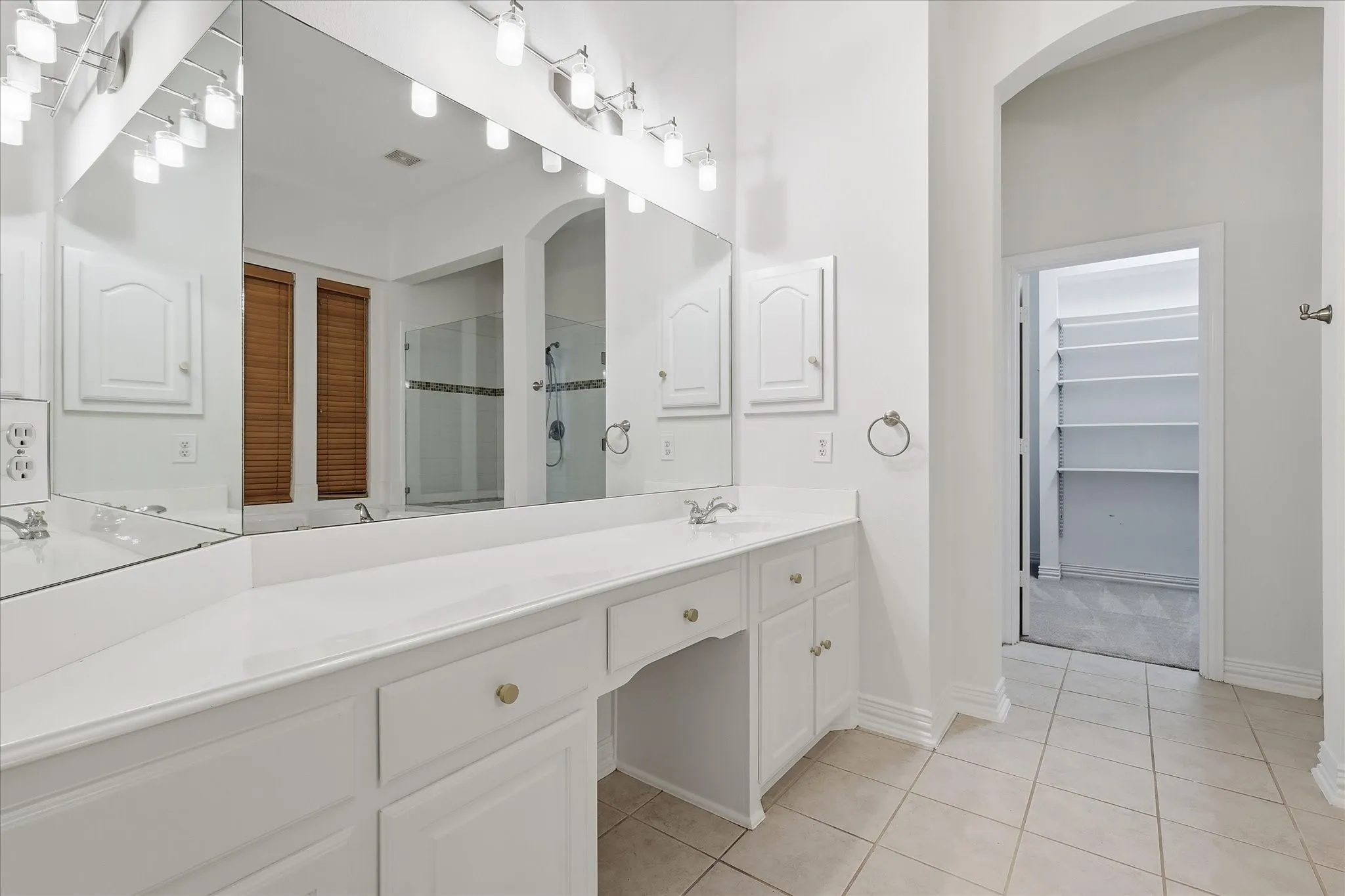 Primary bathroom featuring a corner jetted tub, a glass-enclosed shower with tile surround, a vanity with a sink, wood blinds, and tile flooring