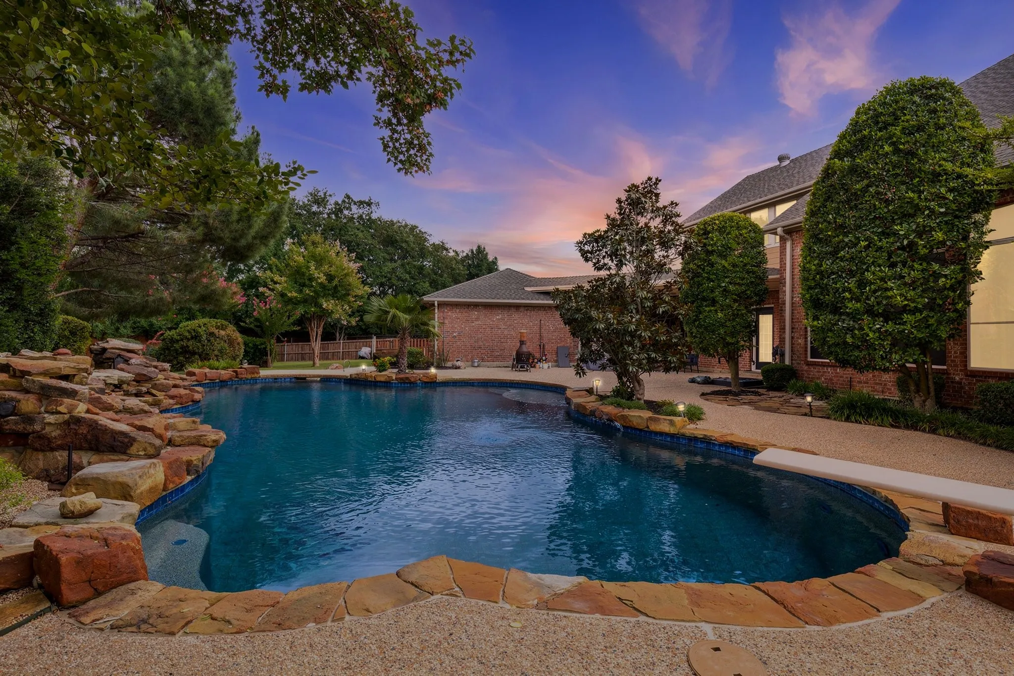Expansive backyard featuring a large swimming pool with a diving board and rock waterfall feature