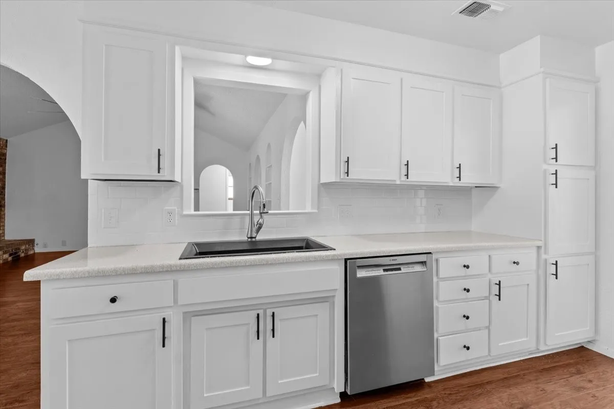 Kitchen featuring white shaker cabinetry, light-colored countertops, a tile backsplash, and a black sink with a gooseneck faucet