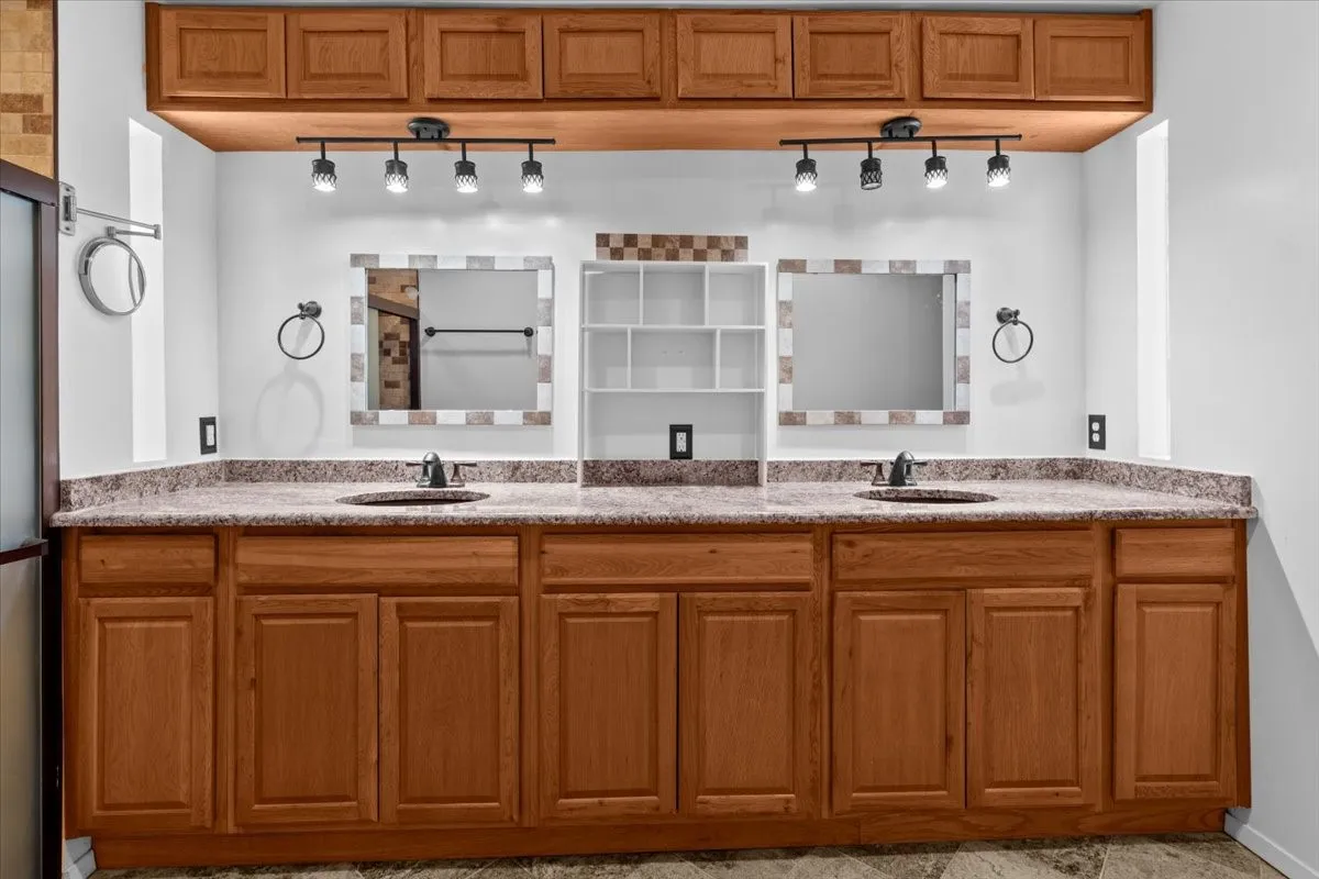 Dual vanity with wood-finish cabinetry, speckled countertops, and track lighting