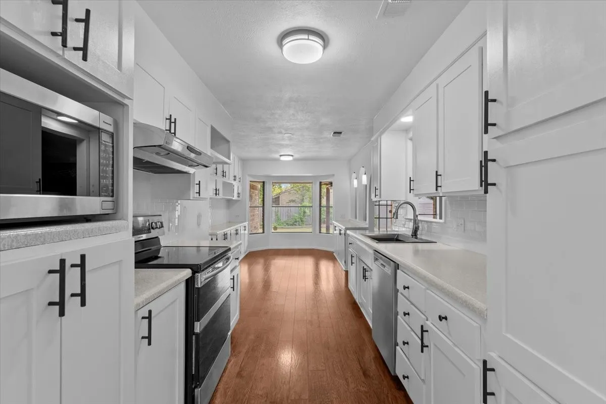 Renovated kitchen featuring white cabinetry, light-toned countertops, stainless steel appliances, wood-finish flooring, and a bay window