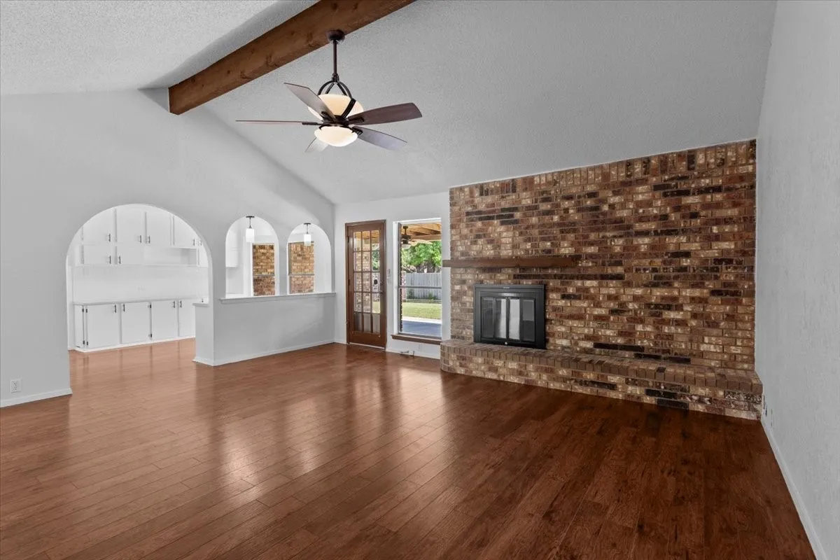 Spacious living area featuring wood-finish flooring, a vaulted ceiling with exposed wood beam, and a ceiling fan