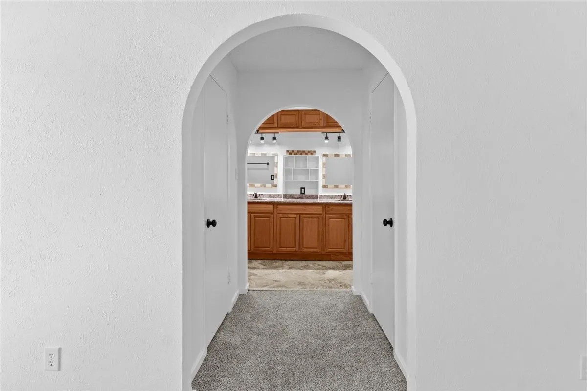 Archway entry leading into a bathroom featuring a double vanity with wood cabinetry, integrated mirrors, and overhead track lighting