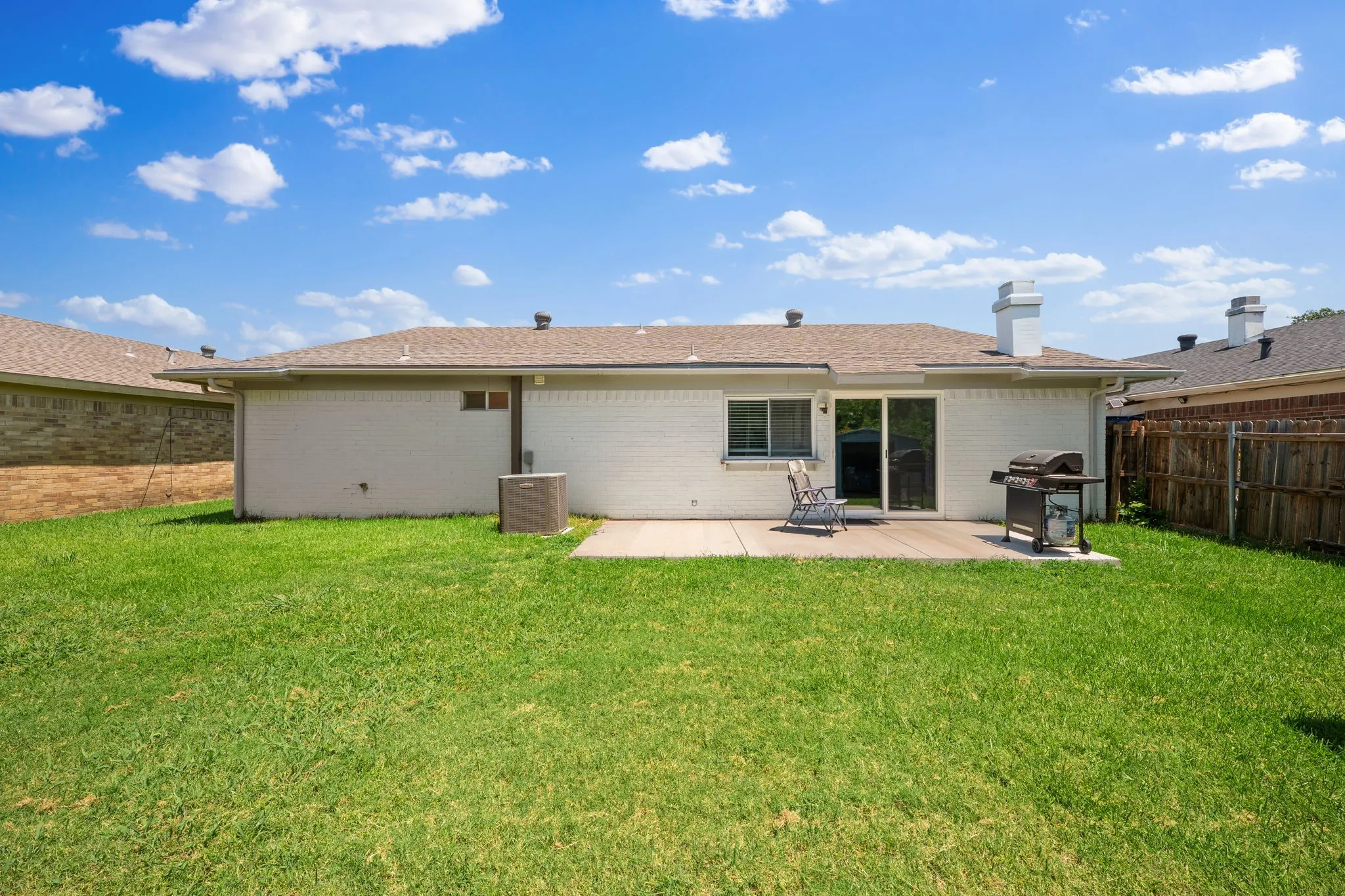 Expansive rear lawn featuring a concrete patio, sliding glass door access, and a durable wood fence boundary