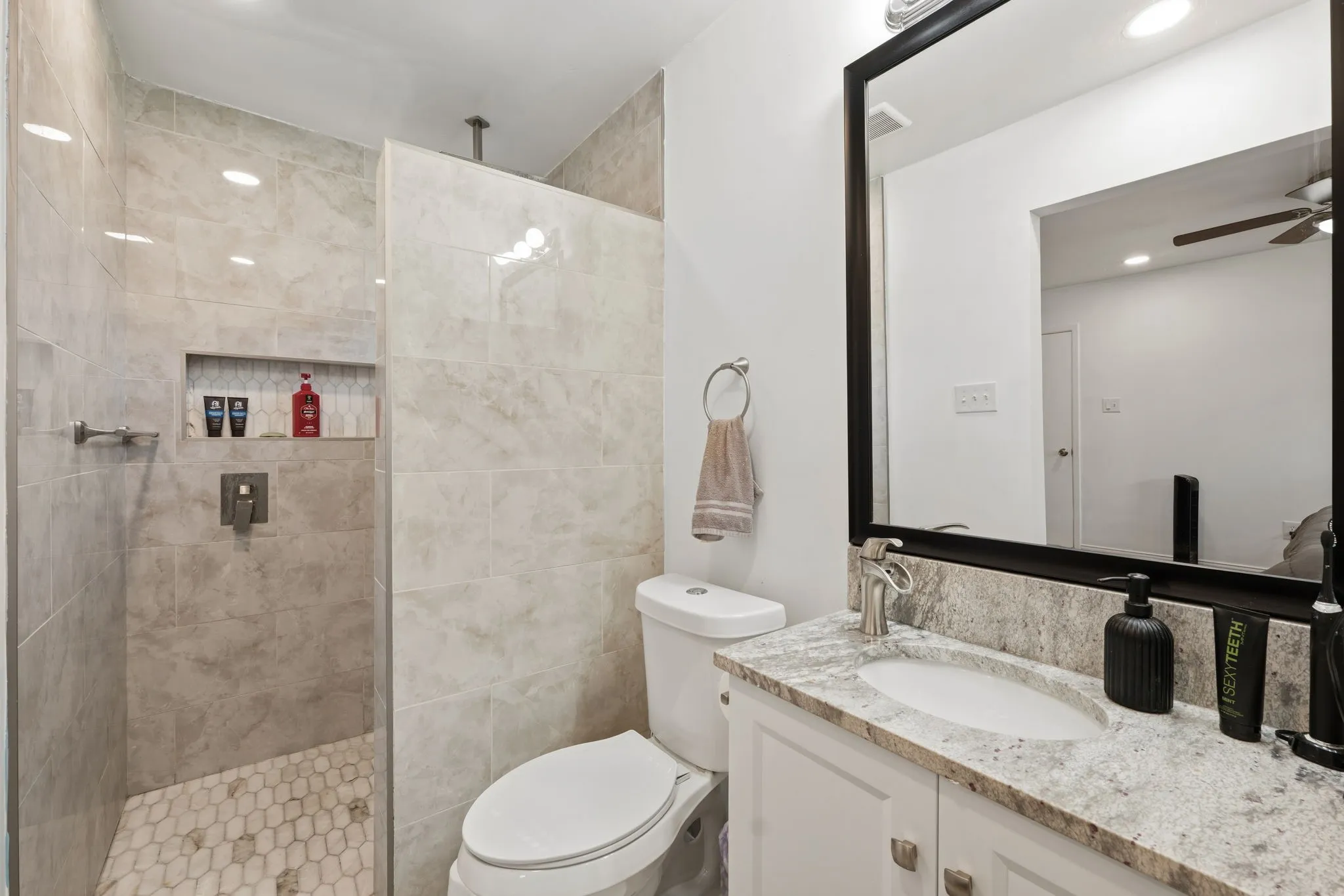 Bathroom featuring a walk-in shower with large format wall tiling and hexagonal floor tiling, a built-in shower niche, and a vanity with a stone-finish countertop and undermount sink