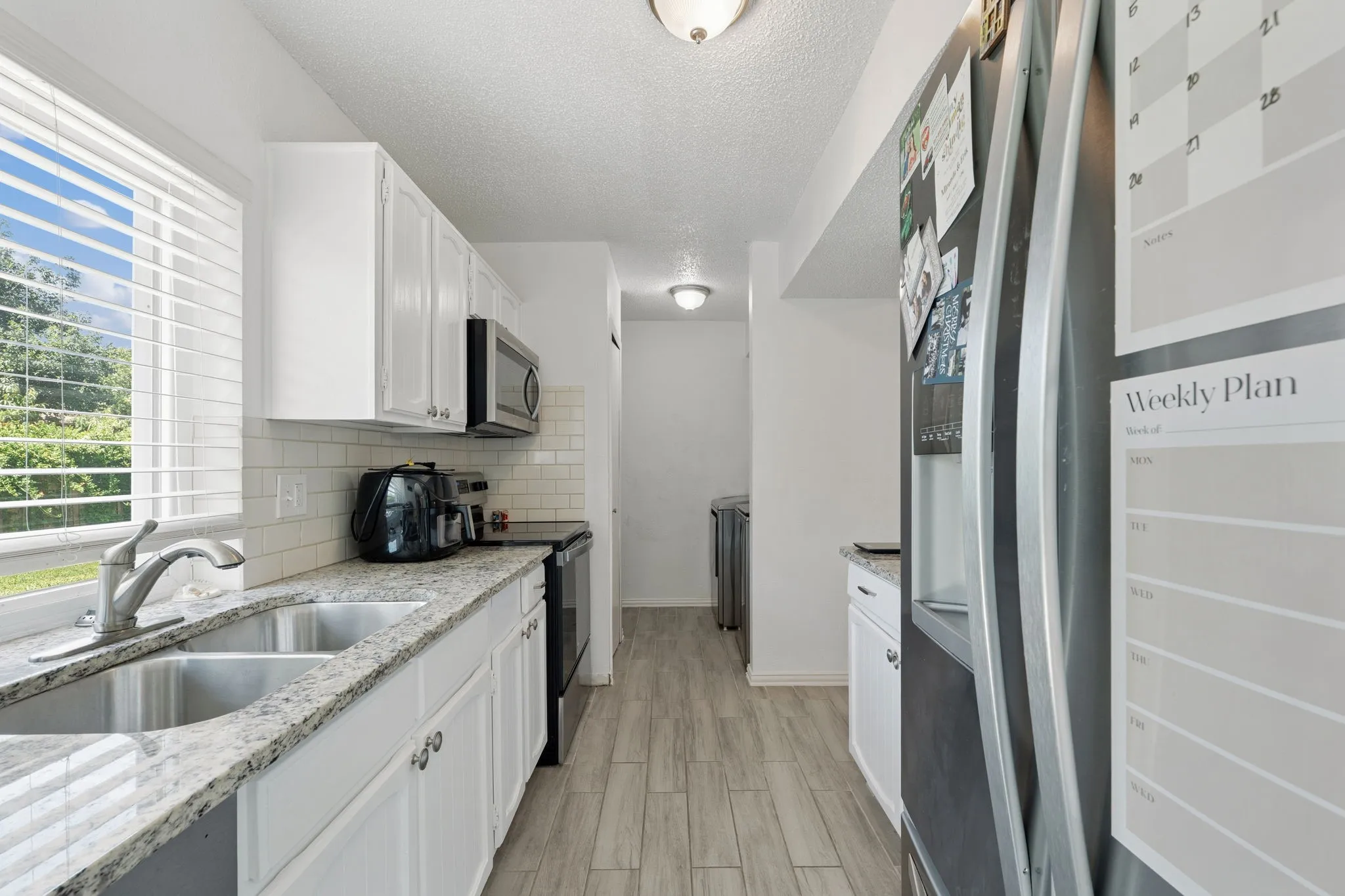 Kitchen featuring white cabinetry, granite countertops, a double stainless steel sink, a subway tile backsplash, and wood-finish flooring