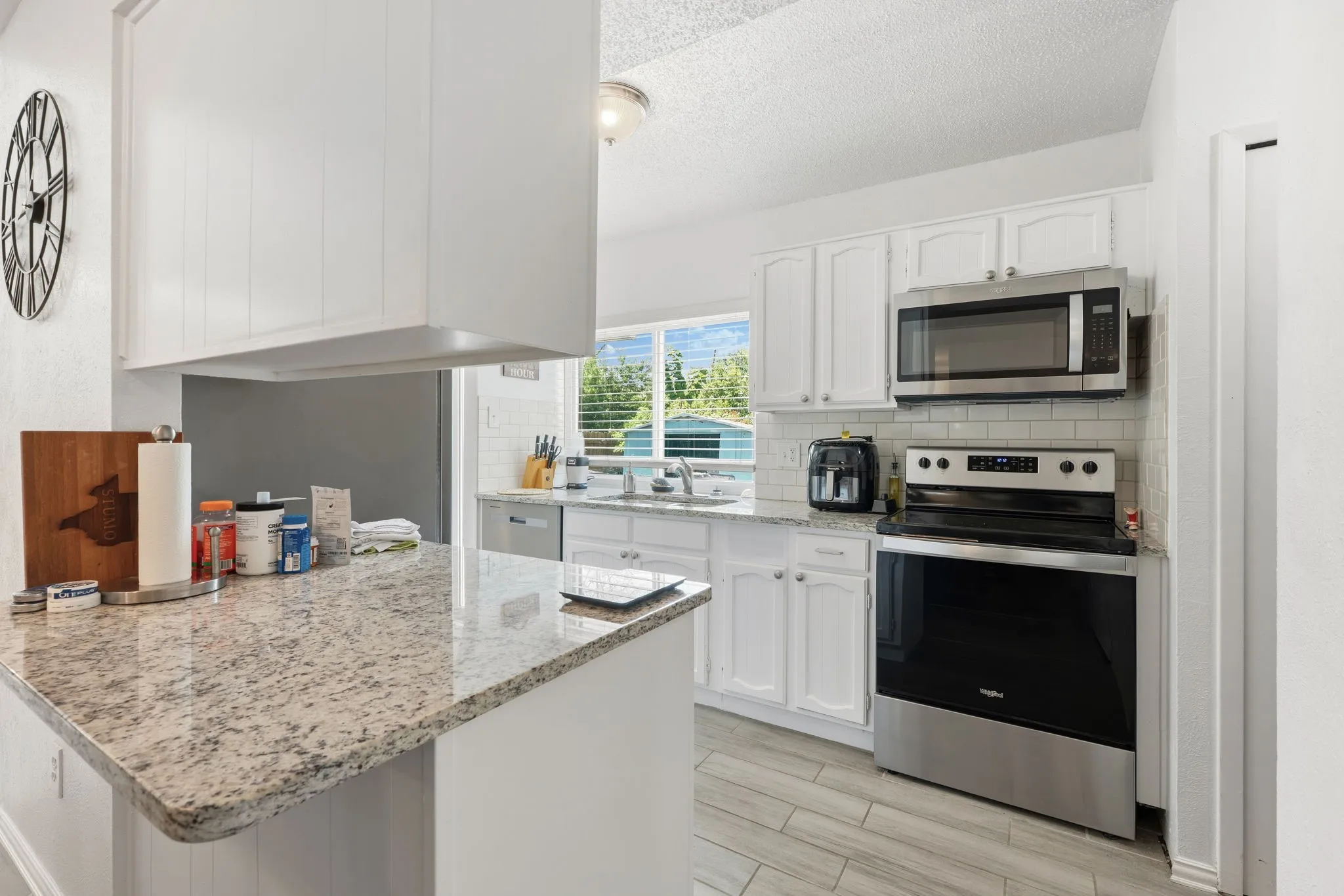 Kitchen featuring white cabinetry, granite countertops, stainless steel appliances, a subway tile backsplash, and light wood-finish flooring