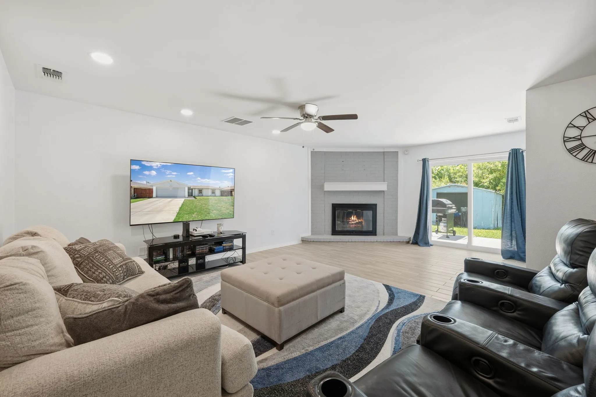 Spacious living area featuring light wood-finish flooring, a corner fireplace with a white mantel, recessed lighting, and a ceiling fan