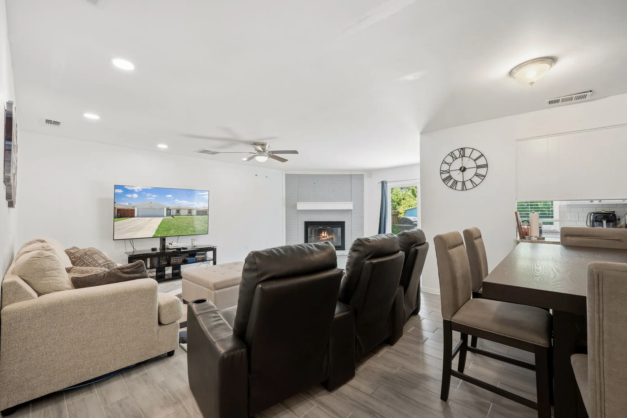 Open-concept living area featuring wood-finish flooring, a contemporary fireplace with a light gray surround, recessed lighting, and a ceiling fan