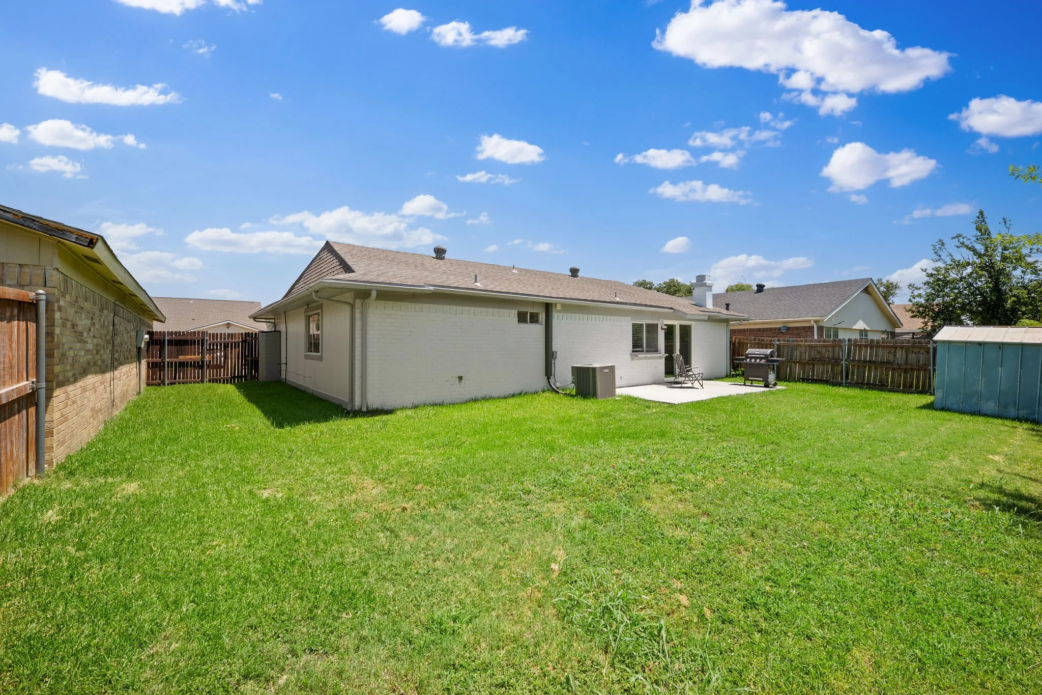 Expansive backyard featuring a manicured lawn, a concrete patio, and mature trees