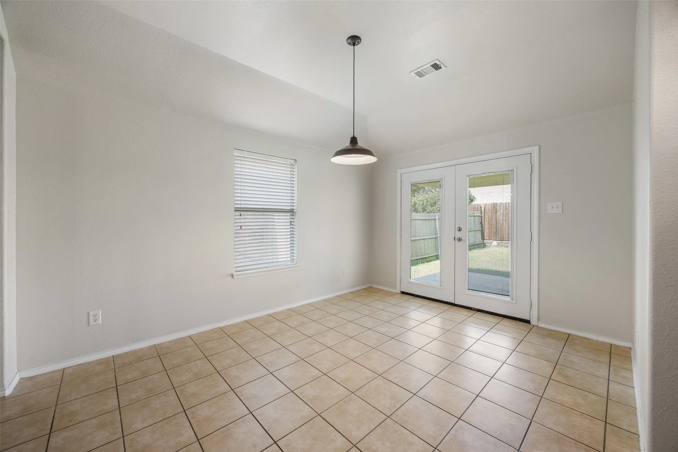 Light-filled room featuring neutral wall tones, tile flooring, a window with blinds, and white French patio doors leading to the outdoor space