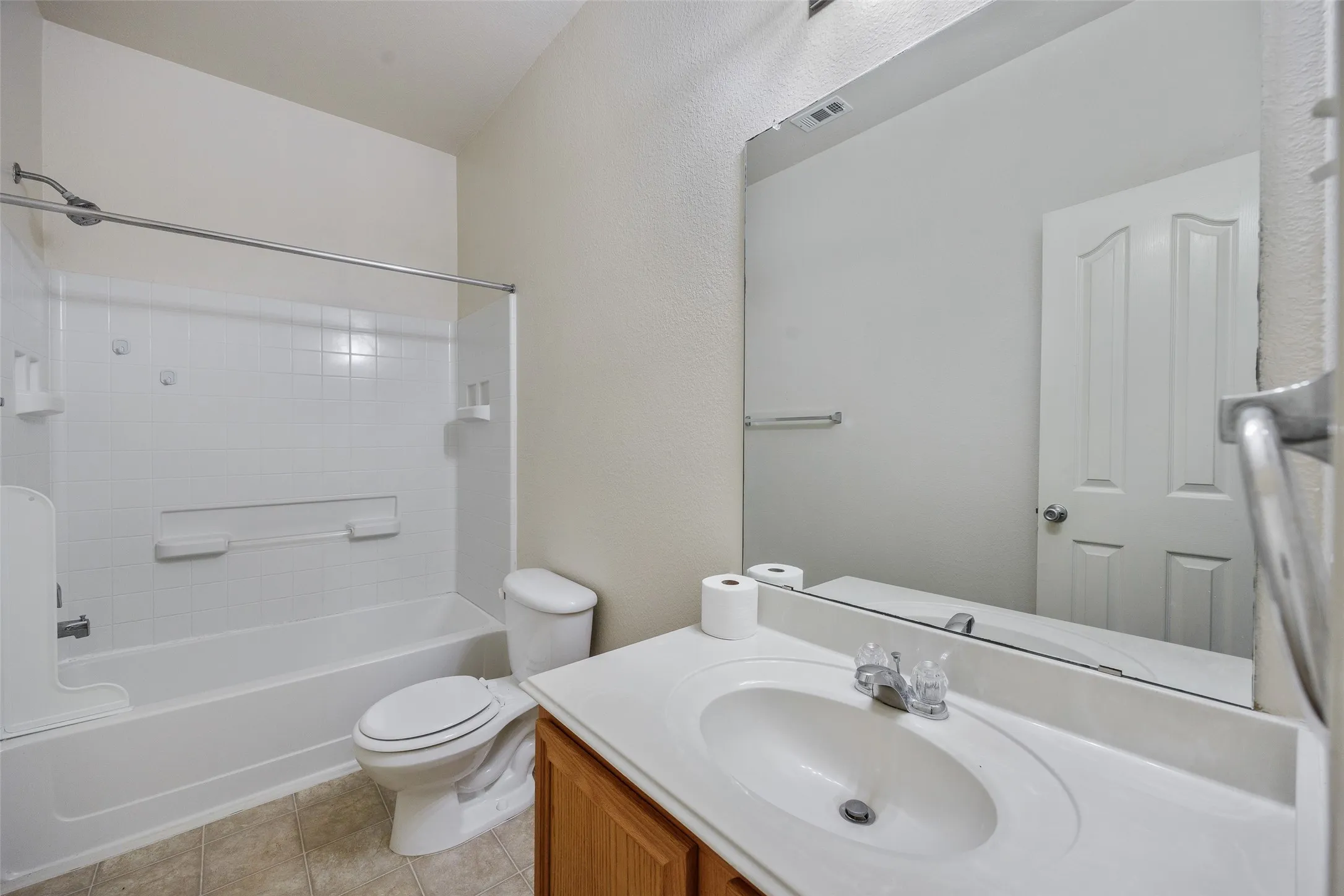 Bathroom featuring a single vanity with a white countertop and oval sink, a large wall-mounted mirror, a standard toilet, and a bathtub with white tile surround